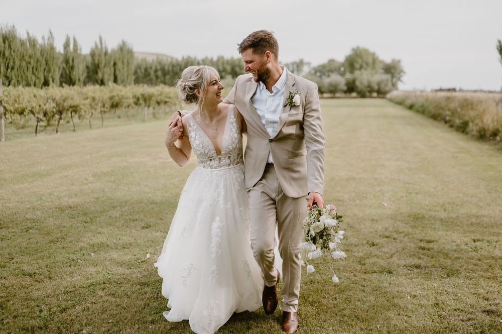 Romantic outdoor wedding photo of couple walking and laughing together in a garden setting.