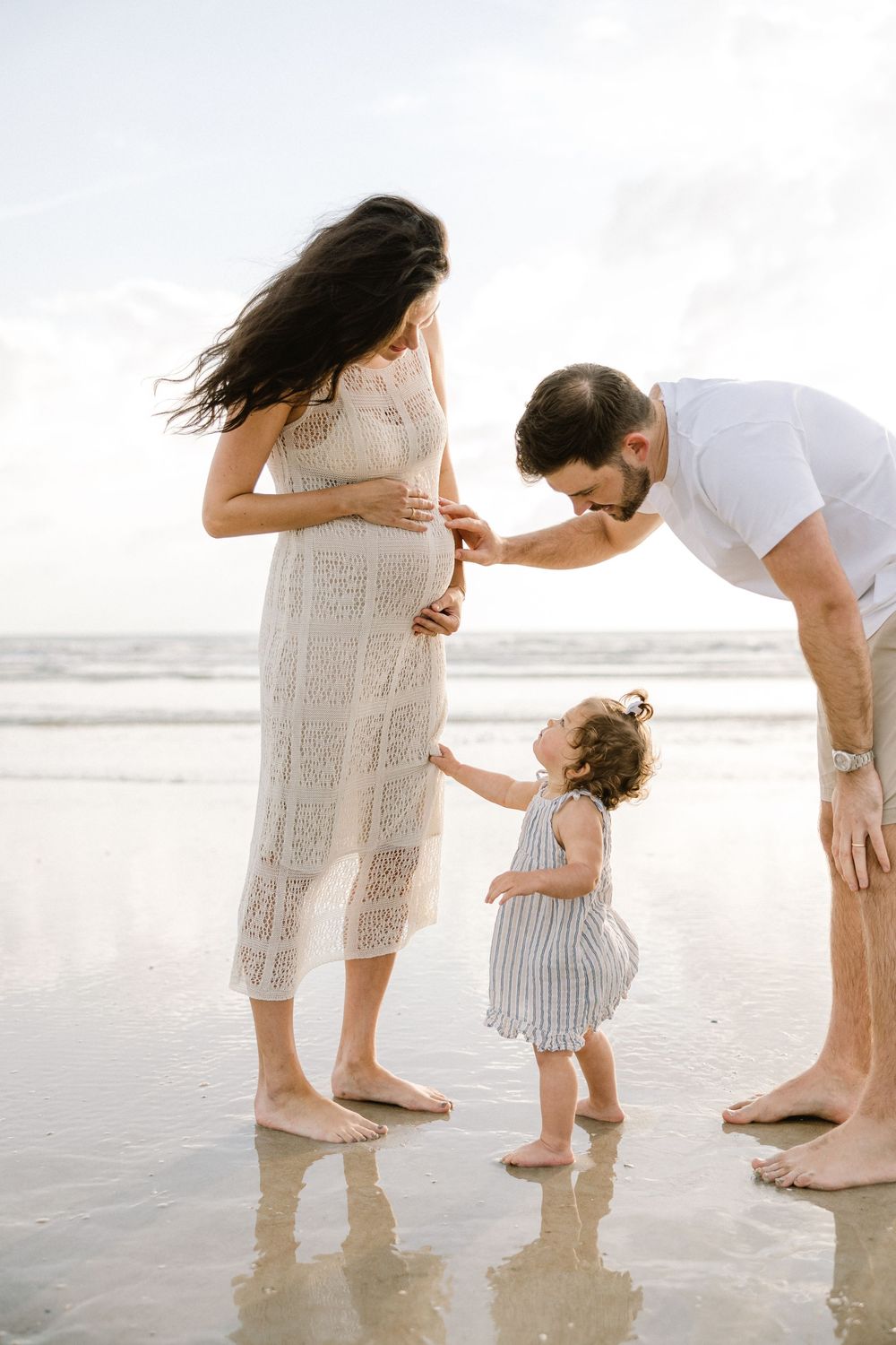 A family shares an intimate moment together on a reflective beach shoreline.