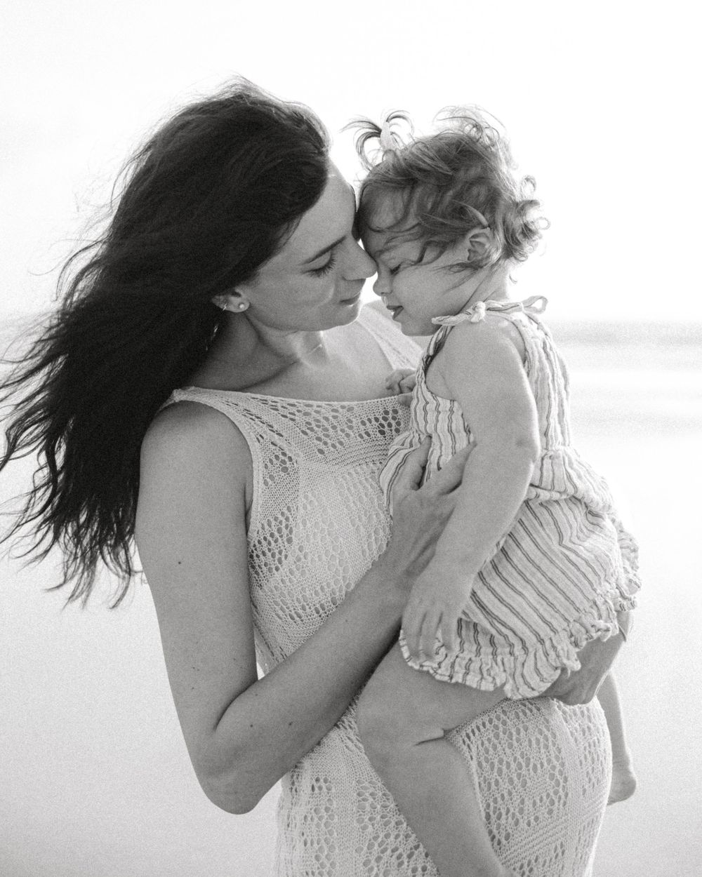 A tender black and white beach portrait capturing an intimate maternal moment.