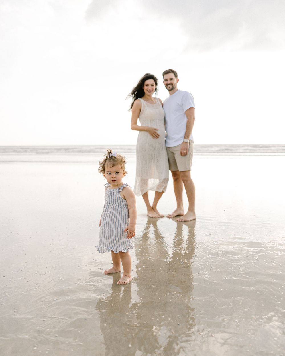 A beachside family portrait with everyone standing in shallow water reflecting the sky.