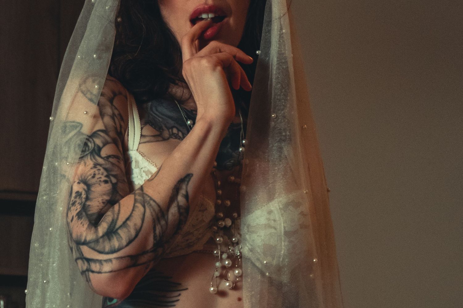 Ethereal portrait through sheer veil showing tattooed arm and soft lighting. bridal boudoir