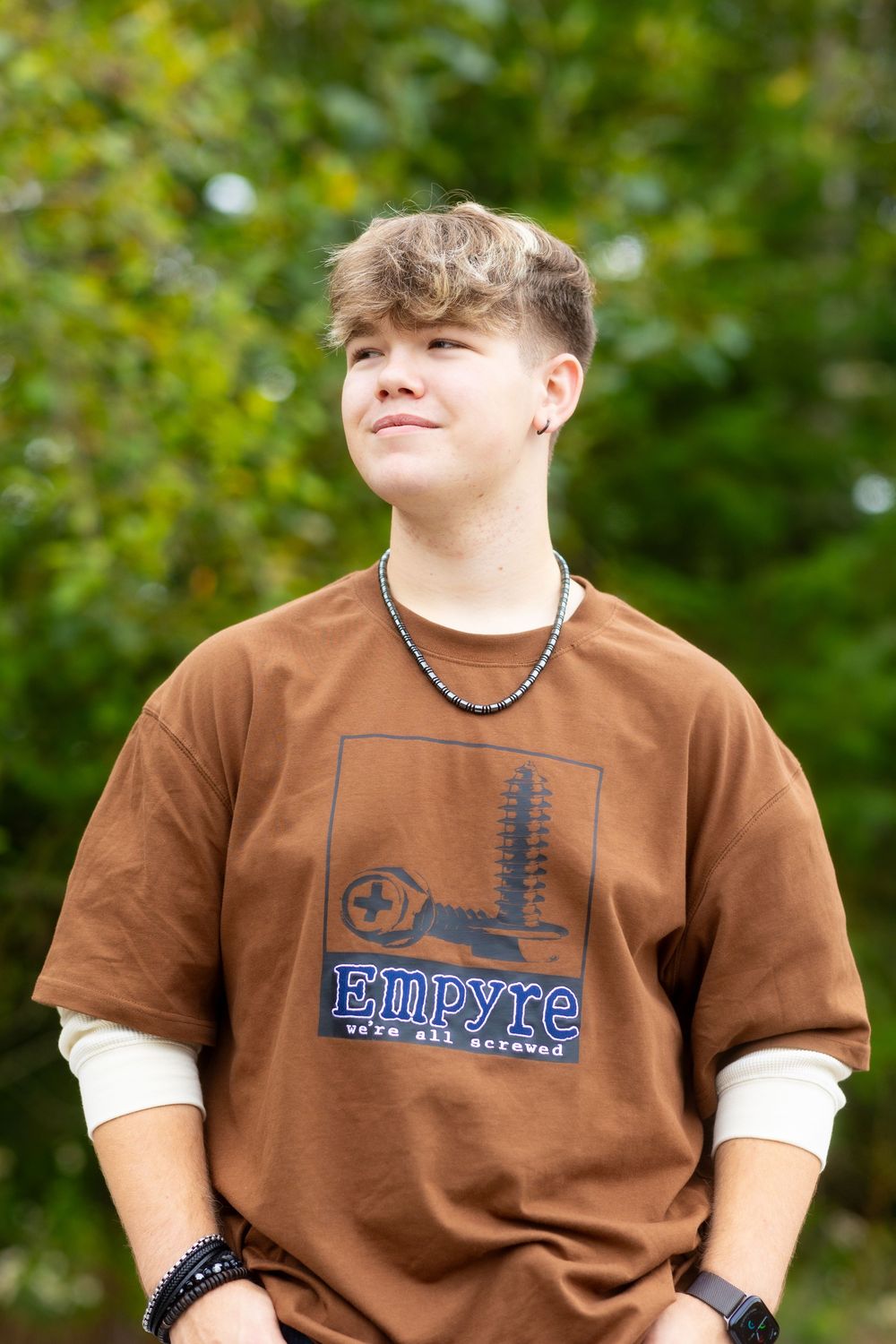 Person wearing a brown t-shirt with football design against green blurred background.