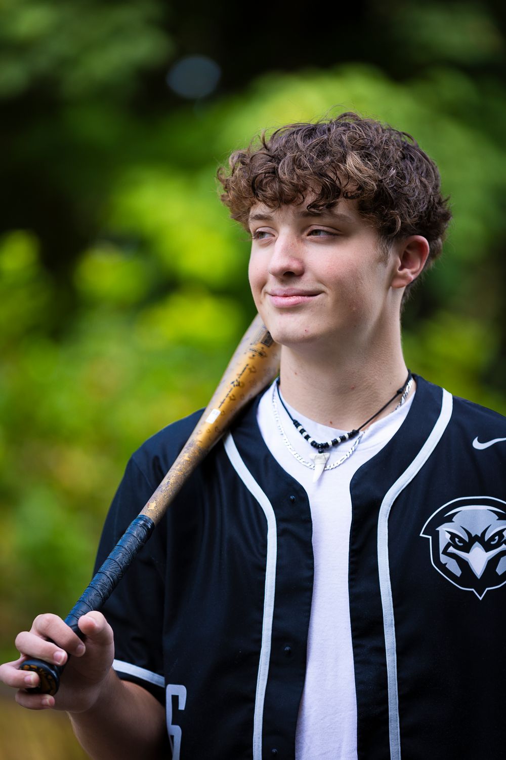 Baseball player in striped jersey posing with bat against green foliage background.