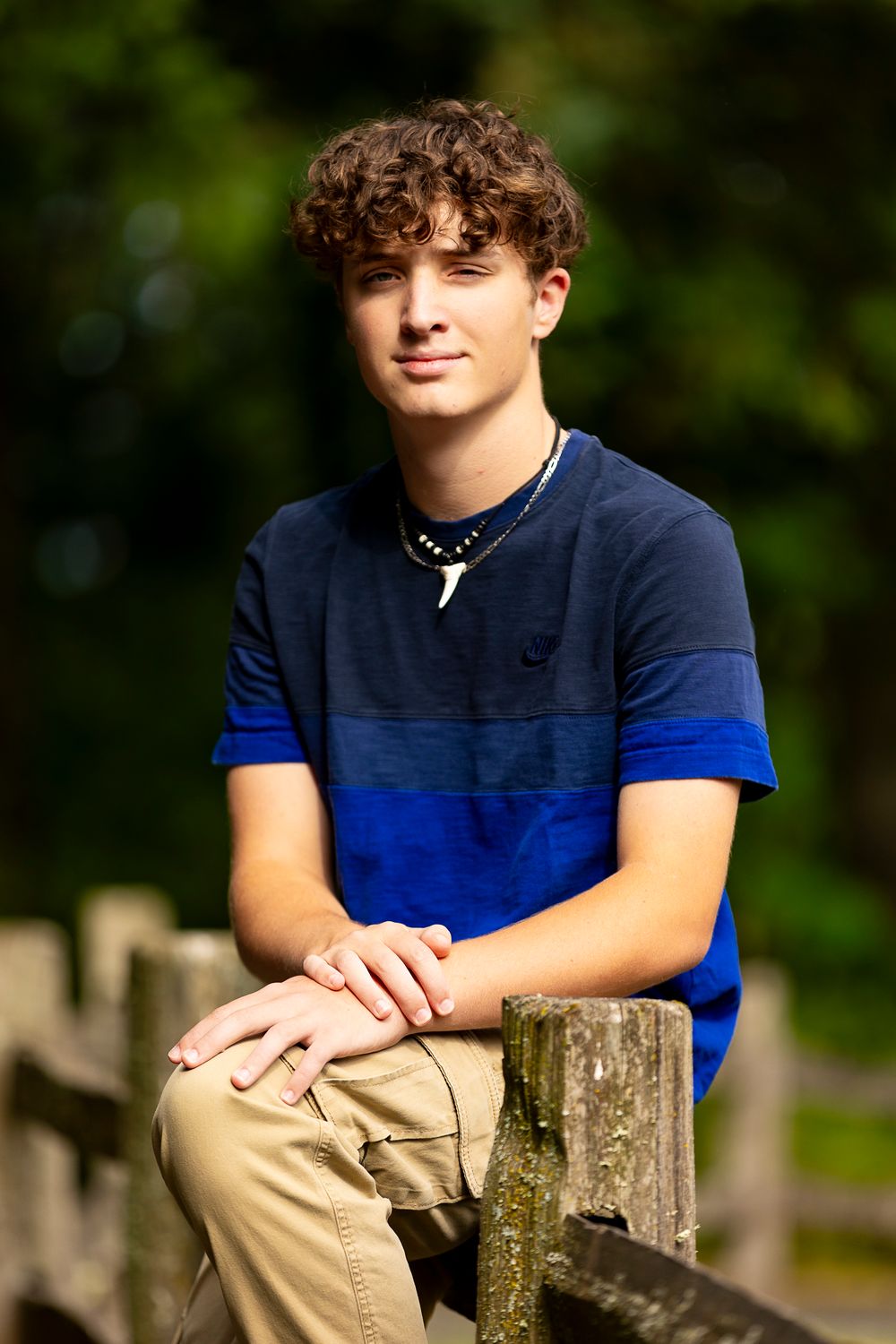 Teen athlete in navy and blue polo shirt leaning on wooden fence post.