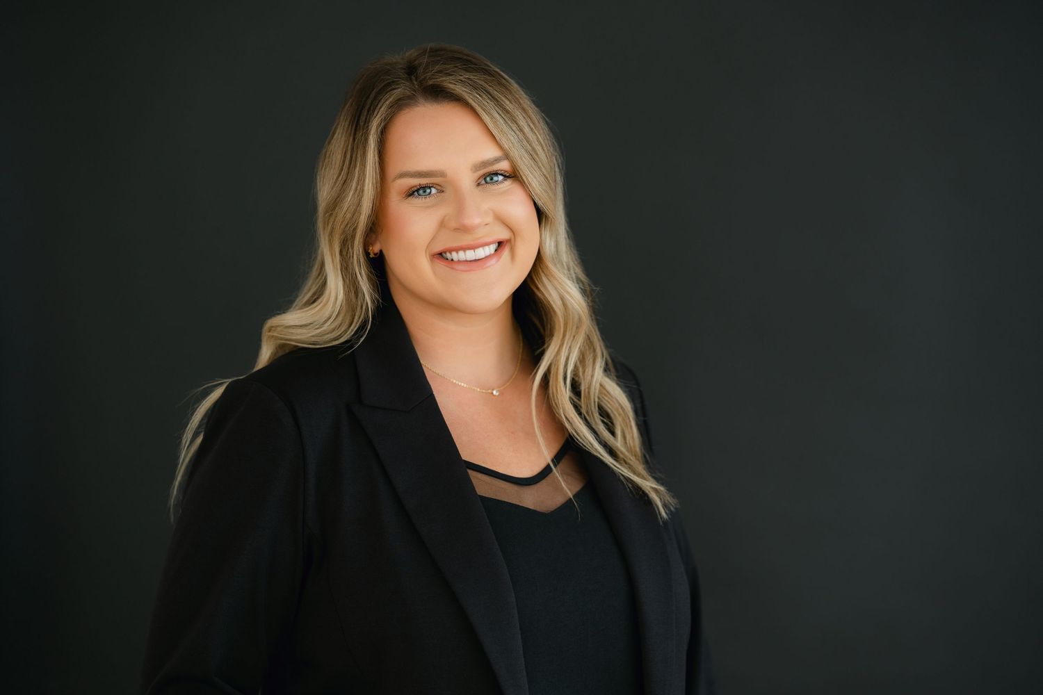 Professional headshot against dark background in business attire.