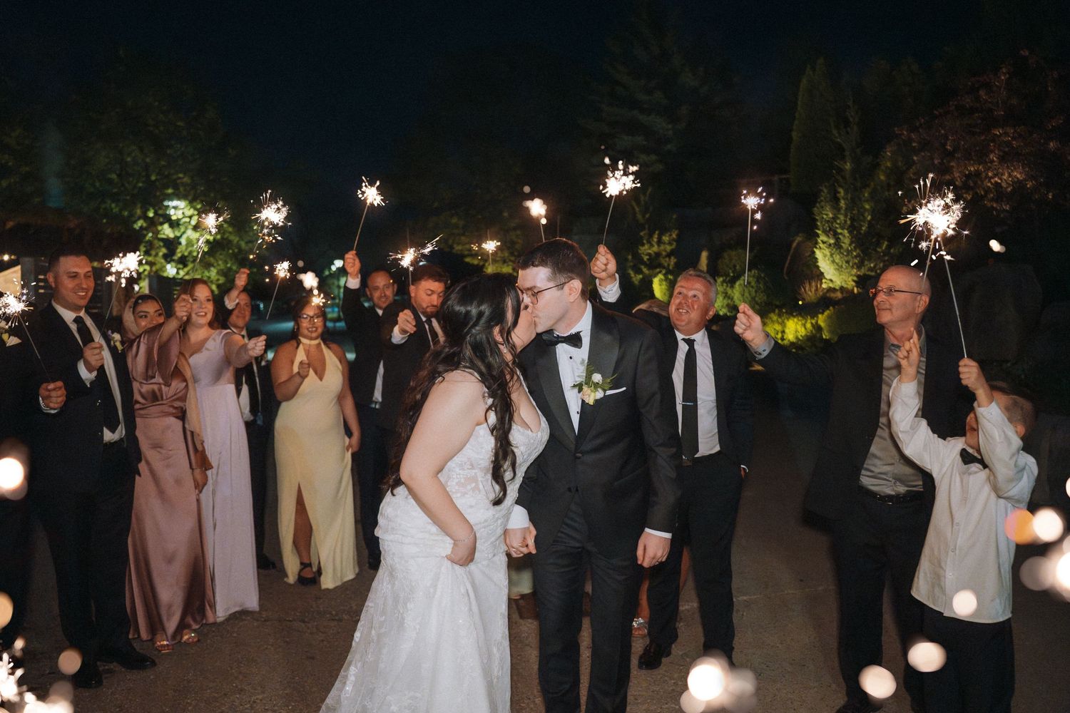 Wedding guests holding sparklers during an outdoor nighttime celebration.