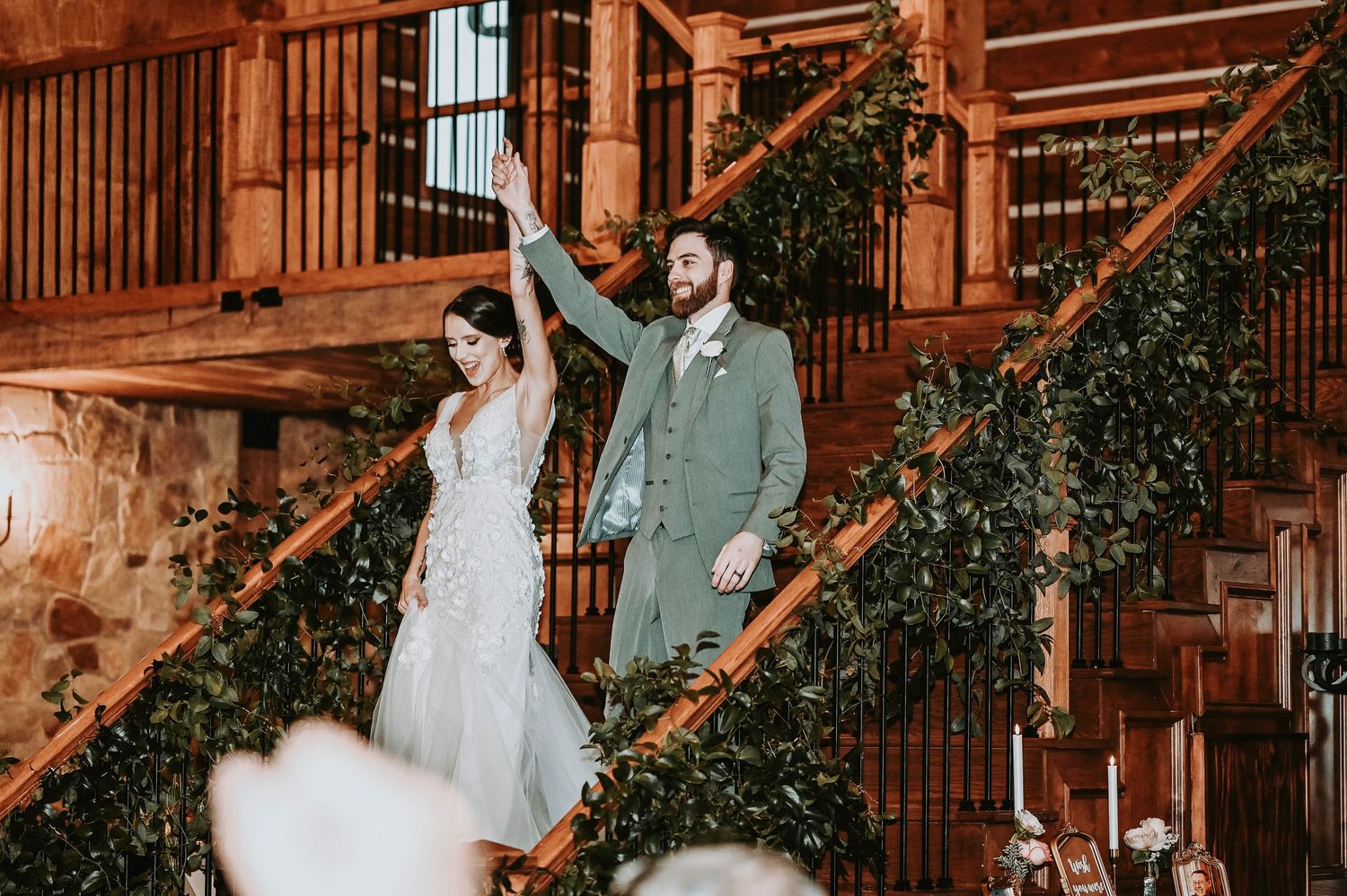 excited bride and groom raise their hands as they walk down the staircase of the lodge at the springs for their grand entrance
