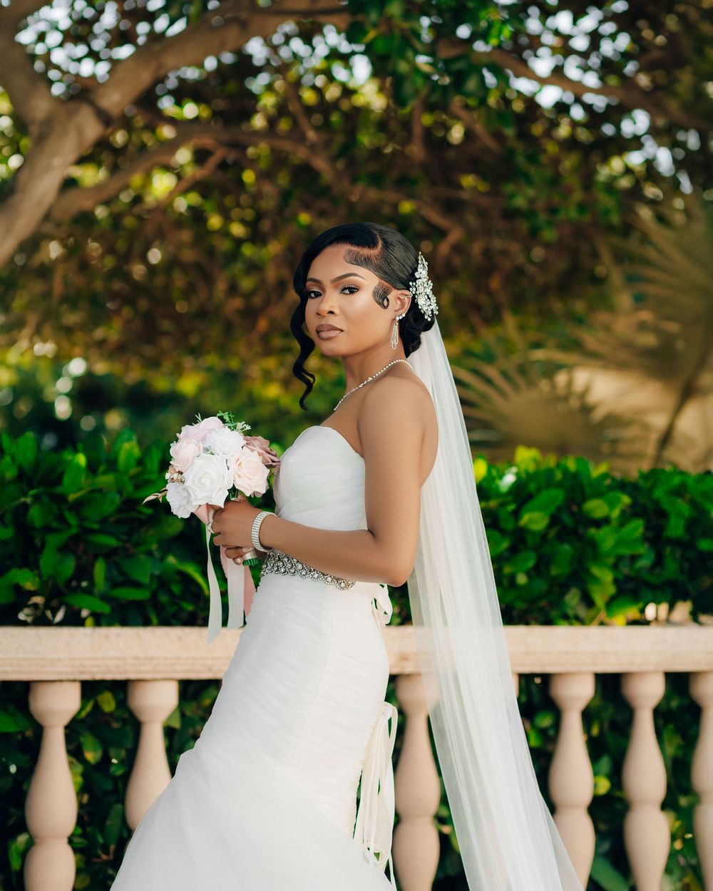 Classic bridal portrait beside stone balustrade with white bouquet and flowing veil.