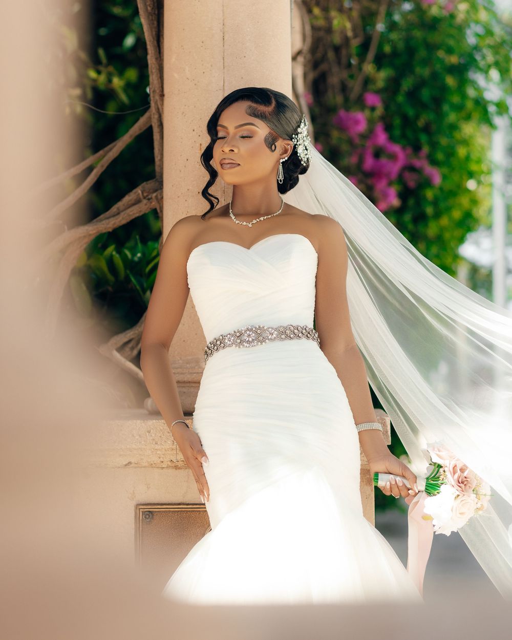An ethereal bridal portrait featuring a flowing veil and form-fitting white gown with embellished waistband.