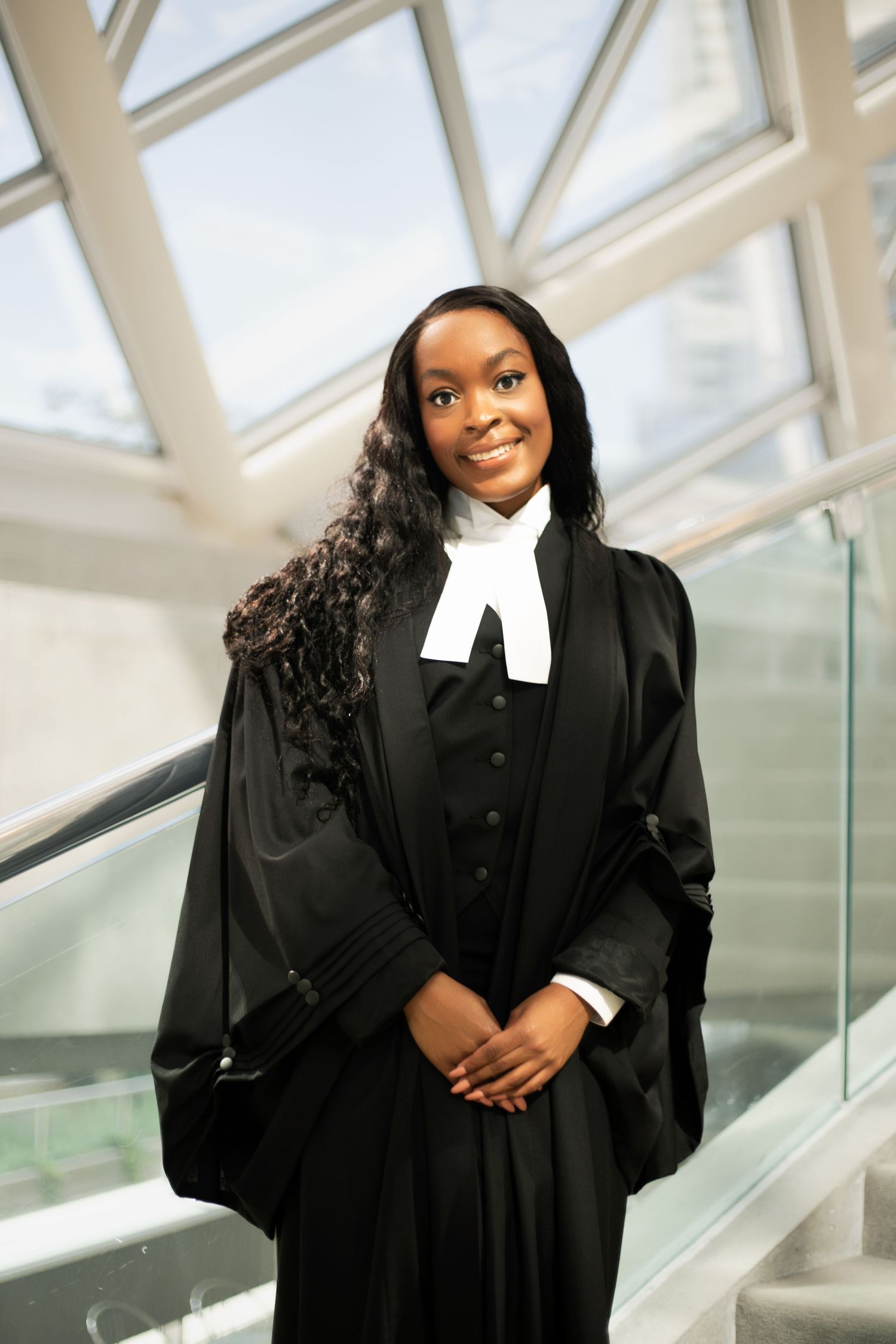 Legal professional wearing traditional barrister attire with white collar band and black gown stands in modern atrium.