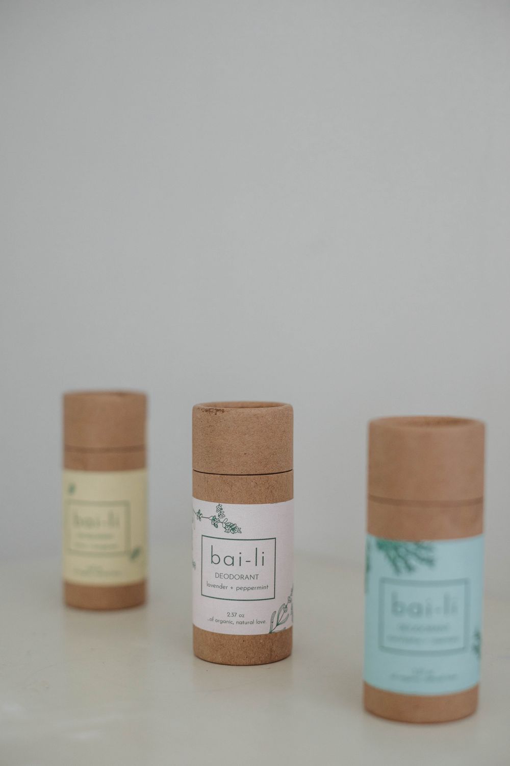 Three natural deodorant sticks with kraft paper packaging and light-colored labels displayed on a white surface.