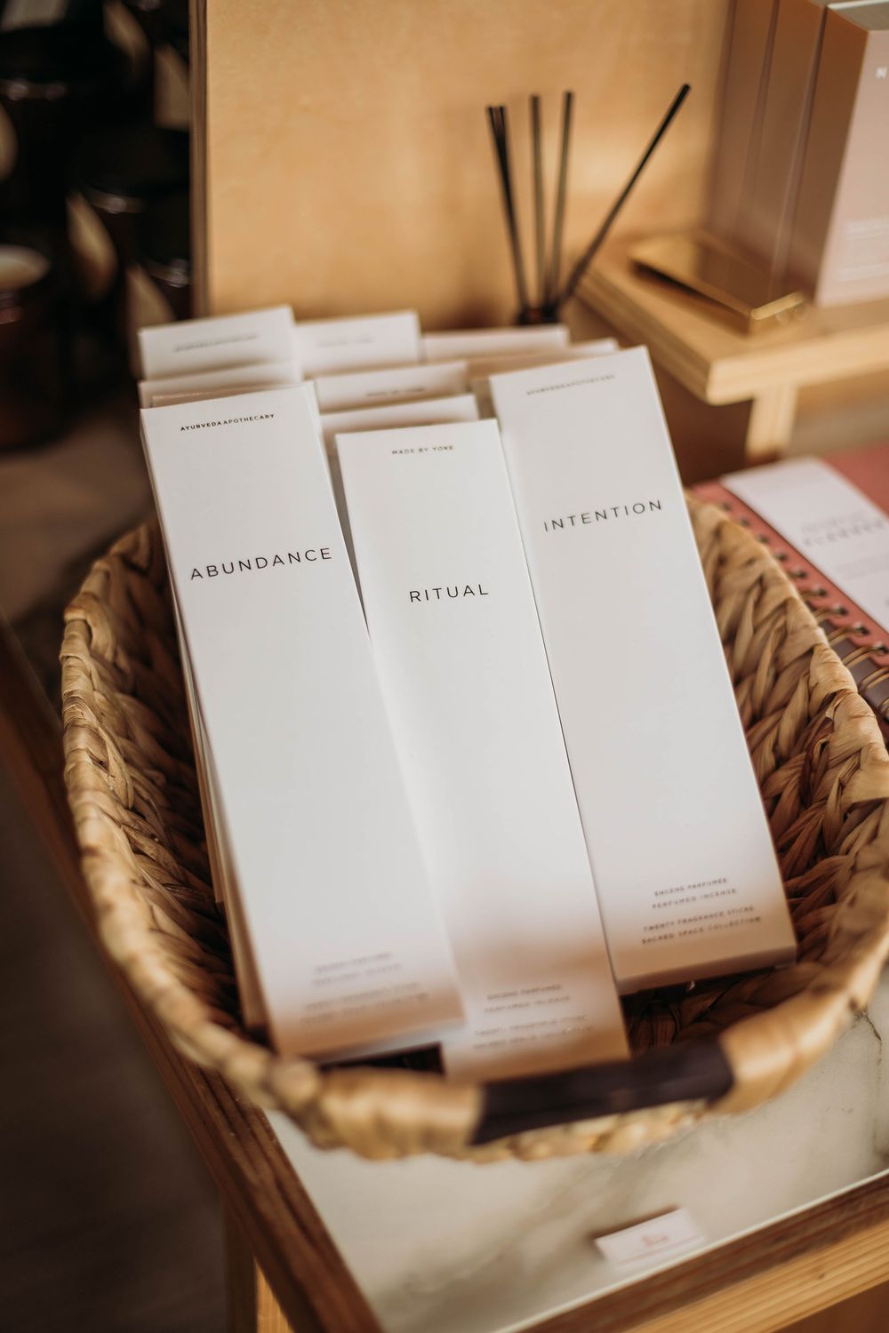 Minimalist white product boxes labeled Abundance, Ritual, and Intention arranged in a woven basket display.