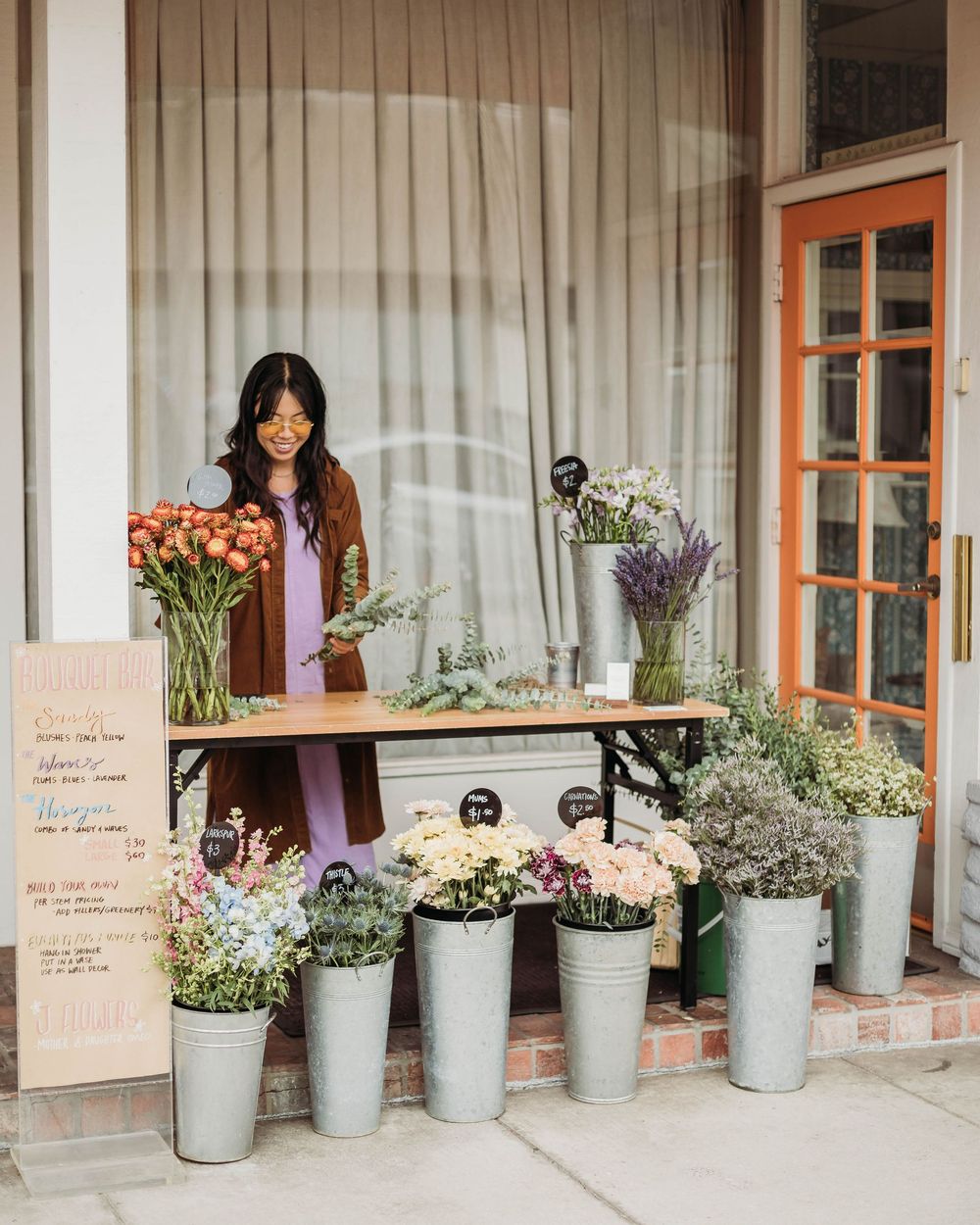 Small local flower shop with rustic storefront display featuring fresh blooms and potted plants arranged on wooden table.