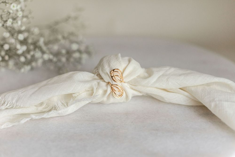 Delicate gold ring on white fabric tied with babys breath flowers in the background.