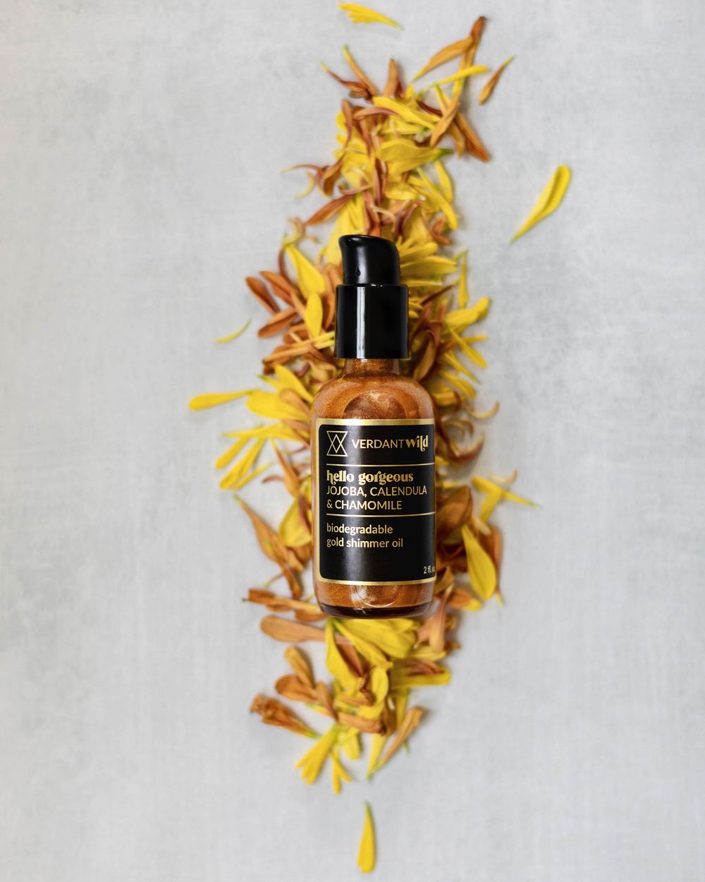 Dark glass bottle of beauty product arranged with scattered yellow and orange dried flower petals on white surface.