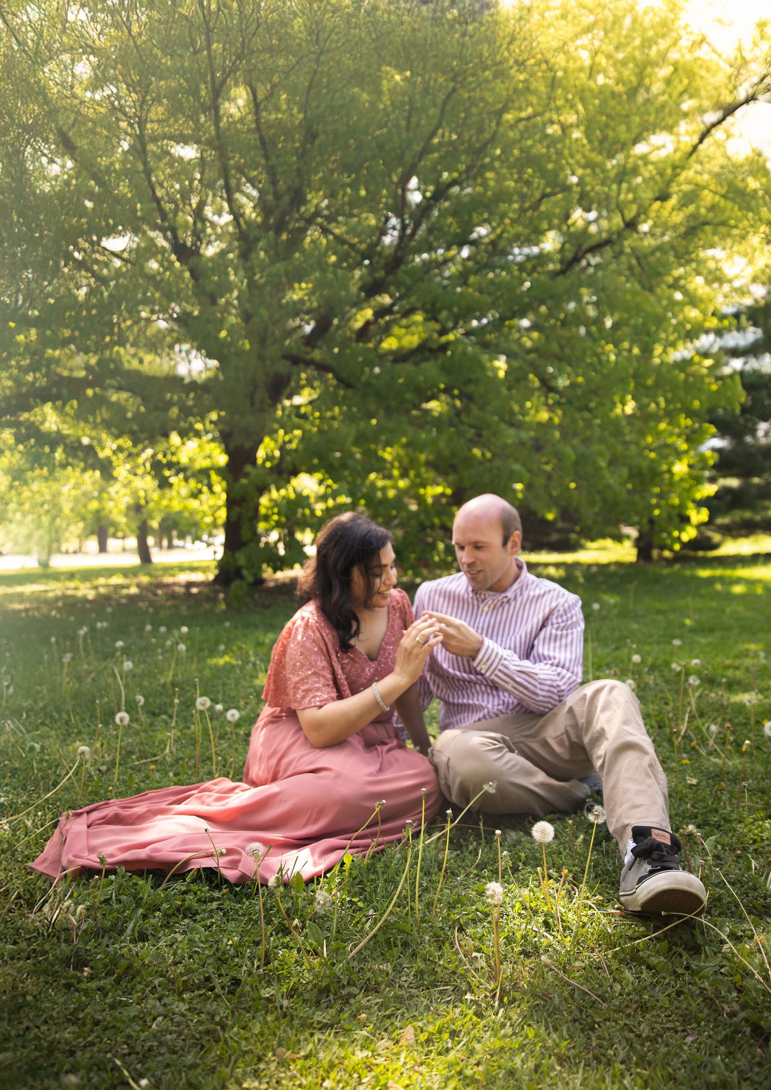 A couple enjoys a romantic sunset moment sitting together on grass in a sunlit park setting.