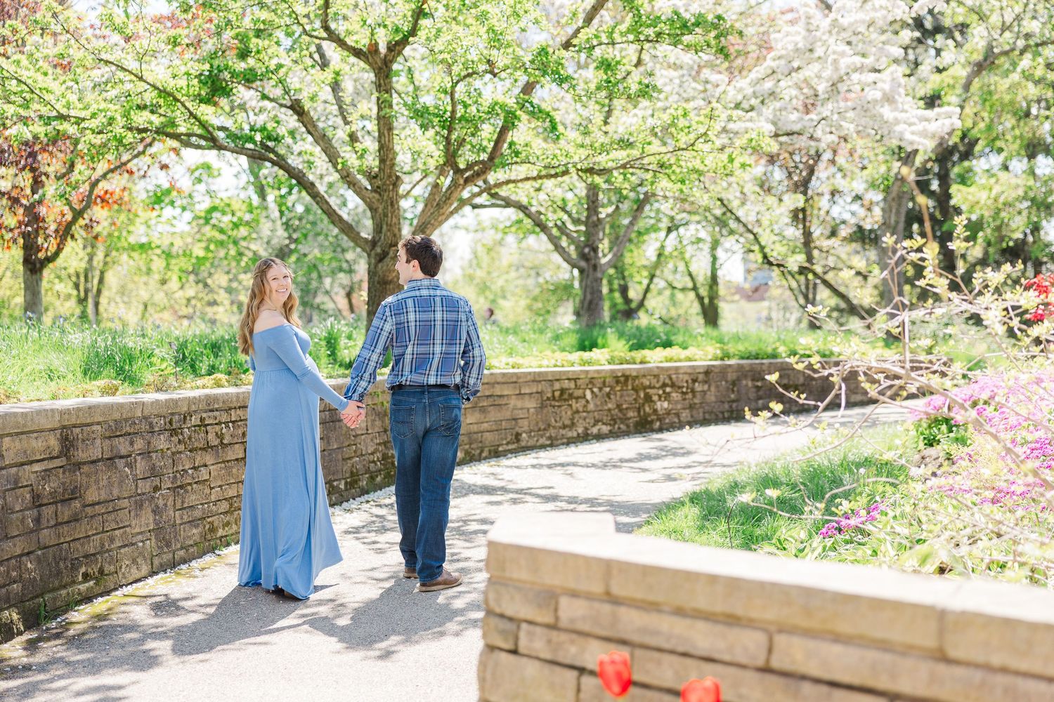 A couple strolls hand in hand along a stone path in a blooming spring garden with cherry blossoms and greenery at Chicago Botanic Garden