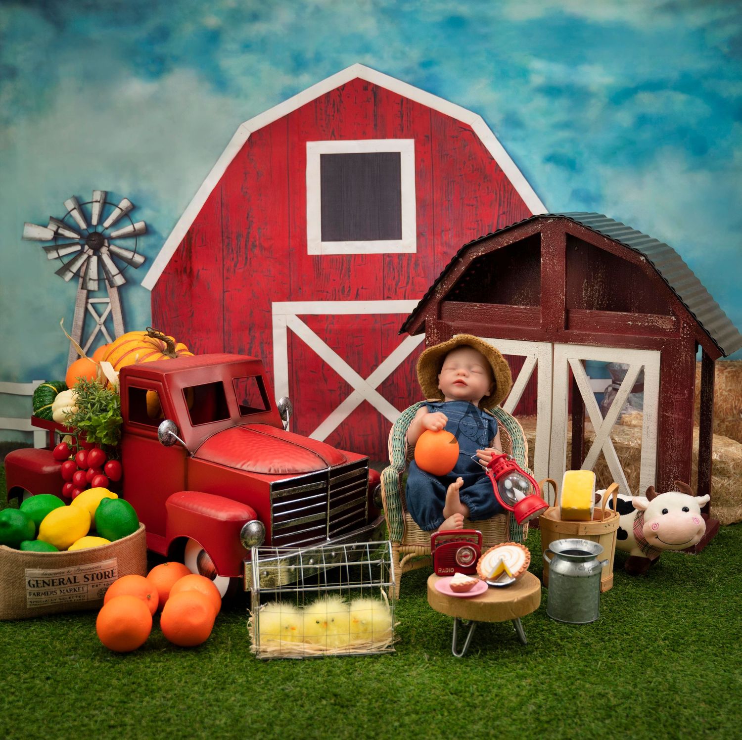 Rustic farm scene with red barn, vintage truck, windmill, and harvest decorations arranged on artificial grass.