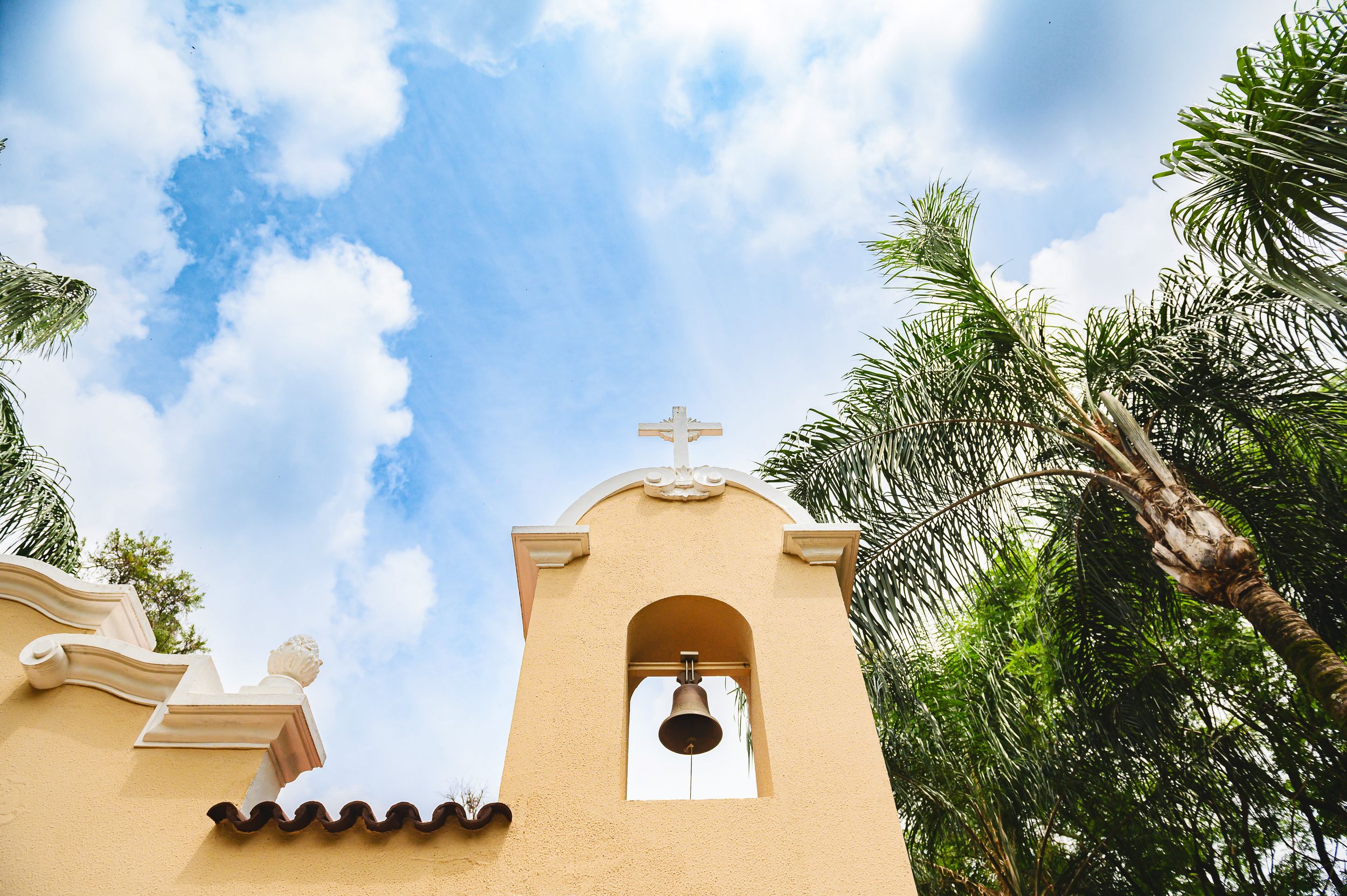 Spanish style church bell tower with terracotta roof against blue sky and palm trees in Florida.