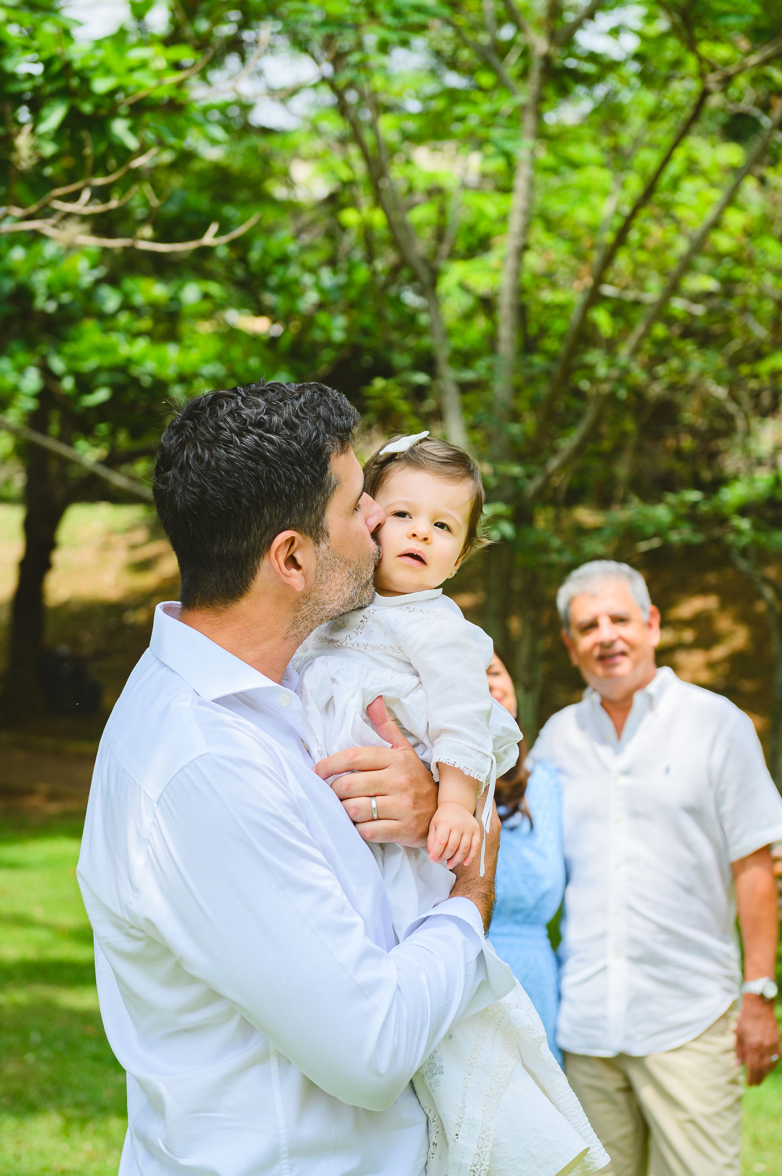 A heartwarming outdoor family gathering shows a warm embrace between parent and toddler while others watch from behind.