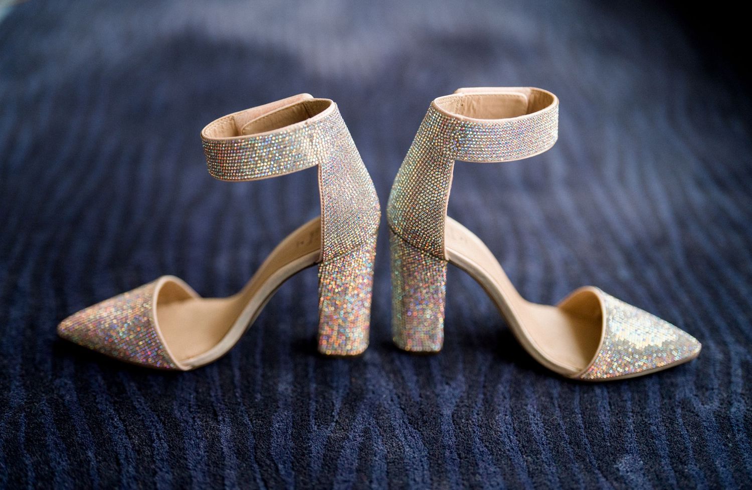 Elegant glittery gold high heel sandals with chunky block heels and ankle straps on dark wooden surface.