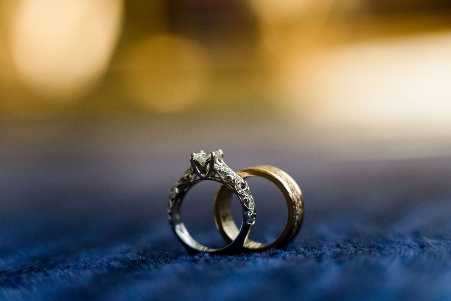Two elegant diamond wedding rings shot in macro with a blurred soft background on blue textile surface.