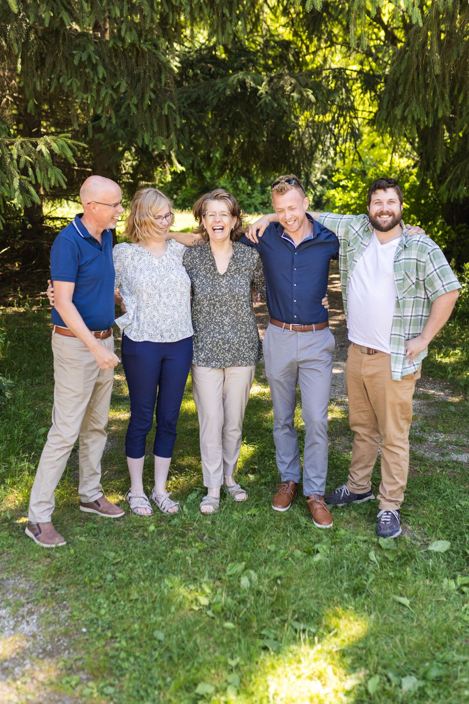 Group of people standing together outdoors on grass with lush green foliage in background on sunny day.
