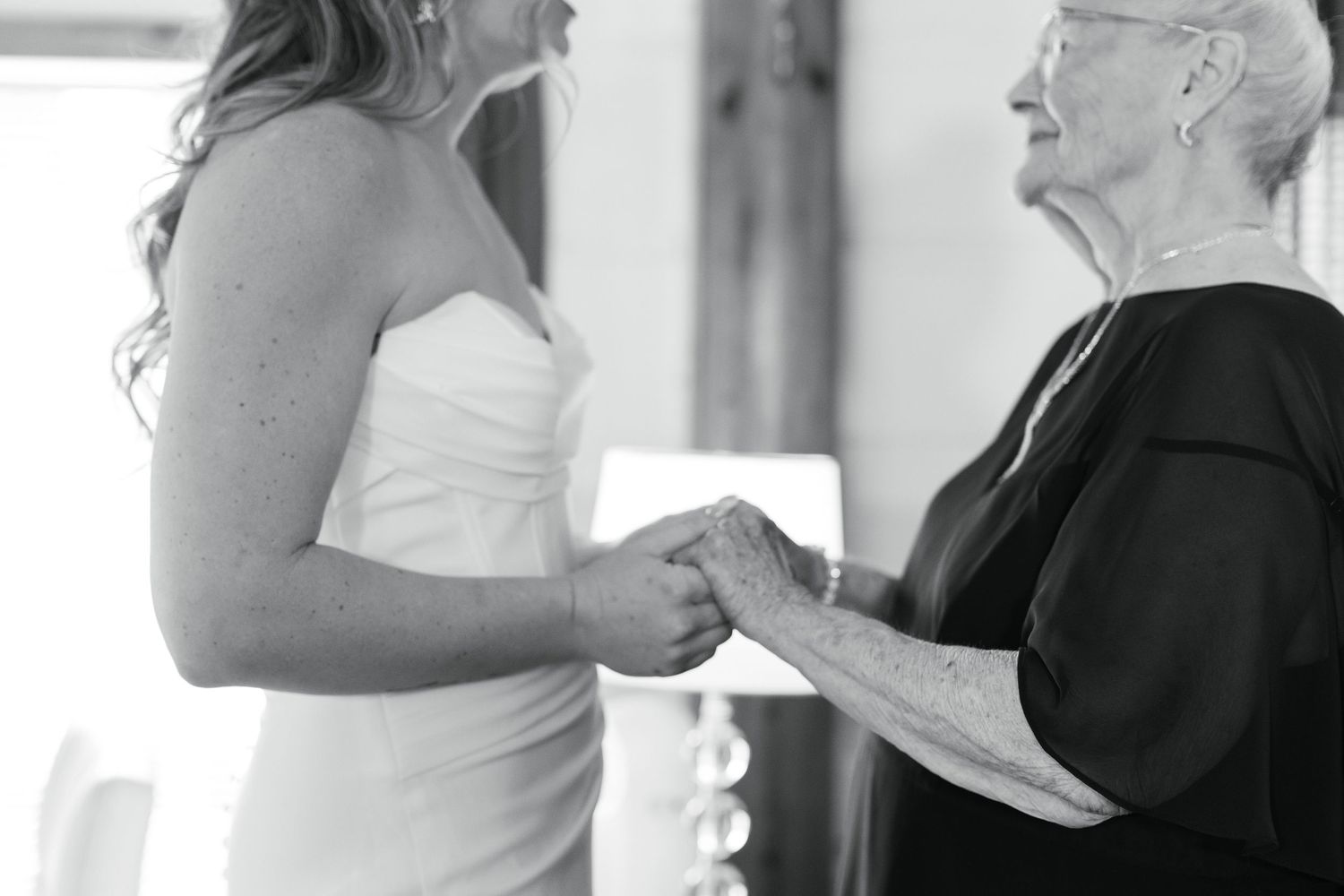 A tender black and white moment showing a bride and older woman holding hands during a meaningful wedding interaction.