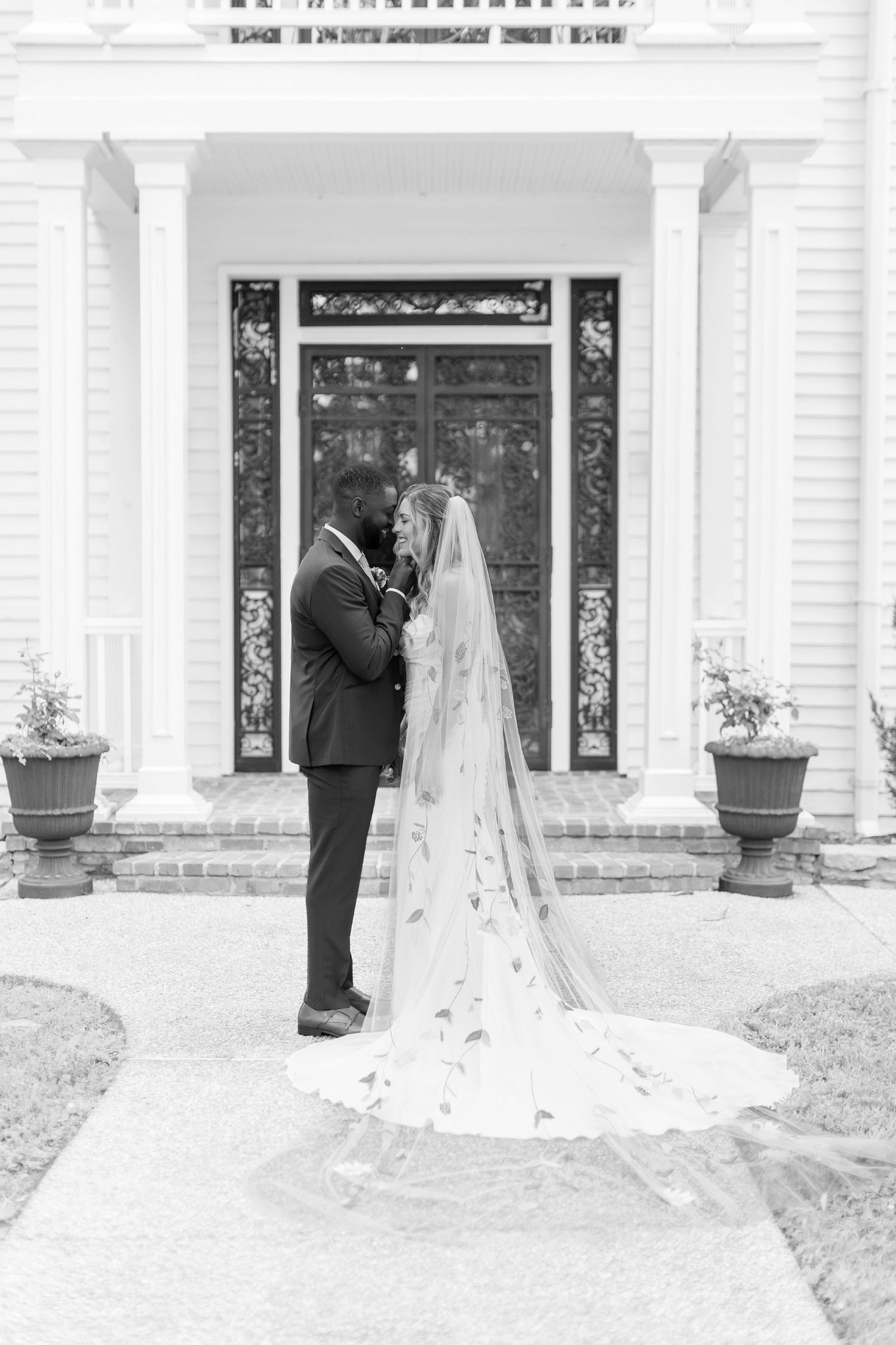 Elegant black and white wedding photo of a couple embracing in front of an ornate doorway with a dramatic cathedral veil.