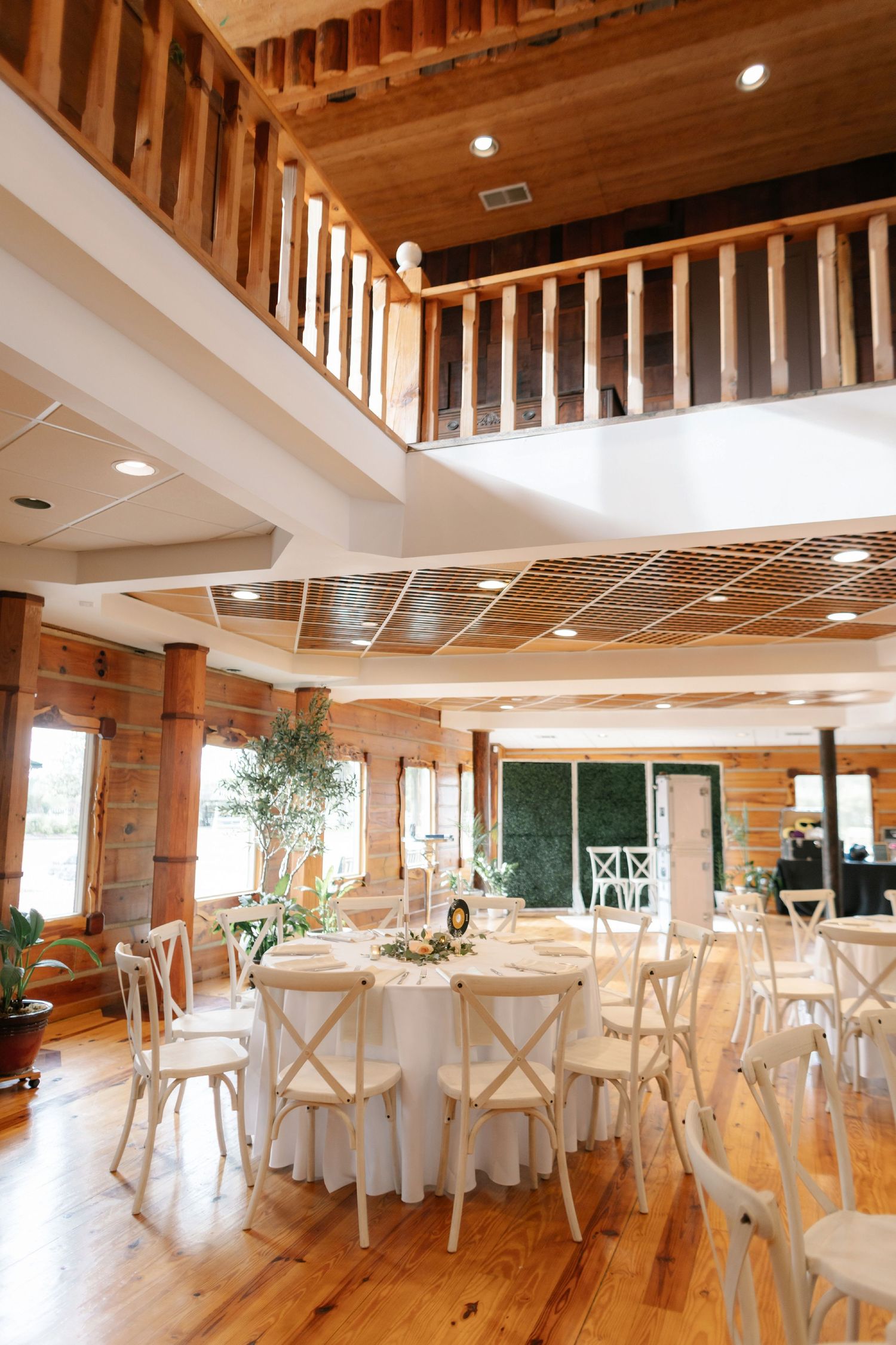 Rustic wooden event venue interior with white cross-back chairs and round tables set for an elegant wedding reception at Legacy Farms.