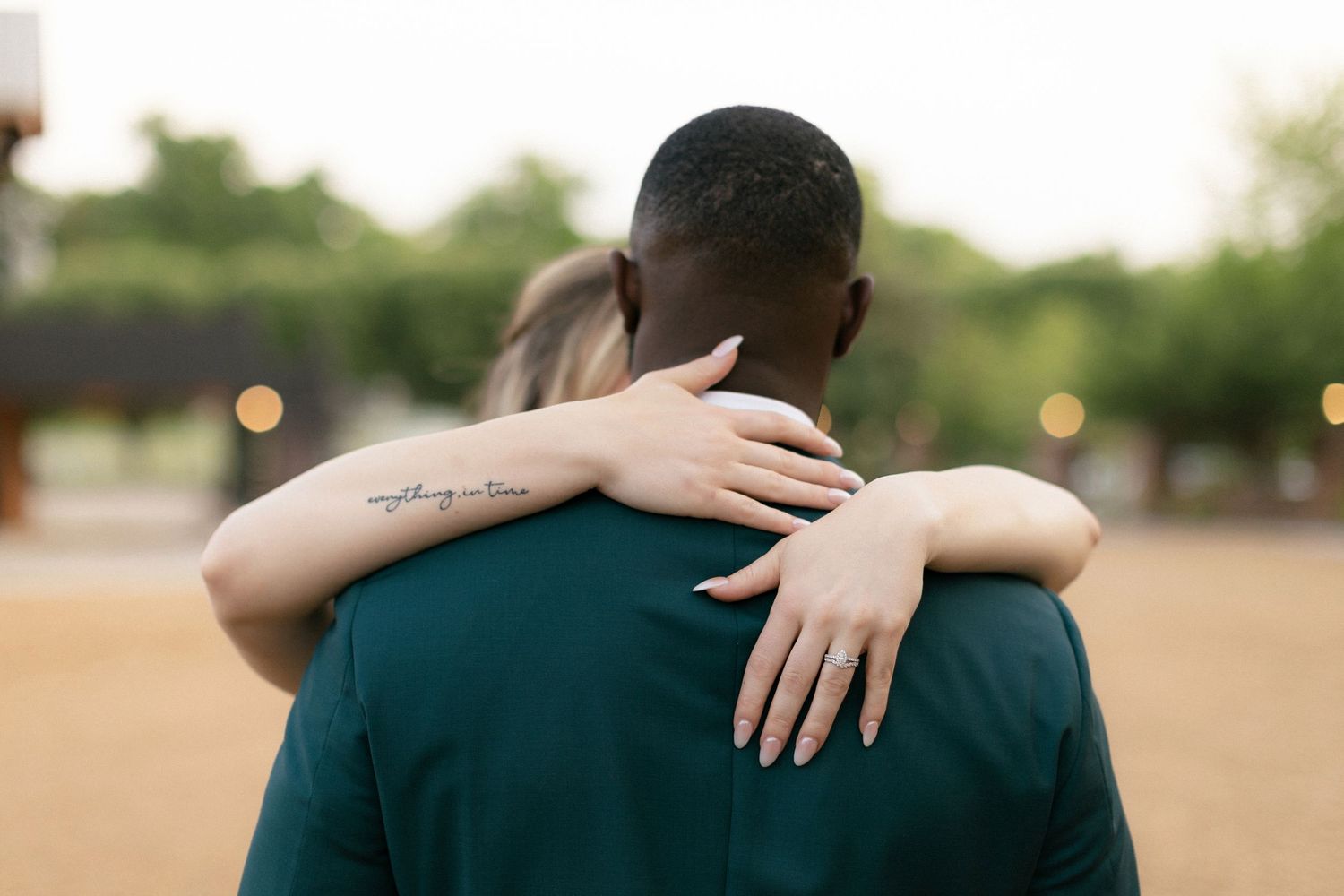 Two people embrace in an intimate hug outdoors with soft bokeh lights in the background.