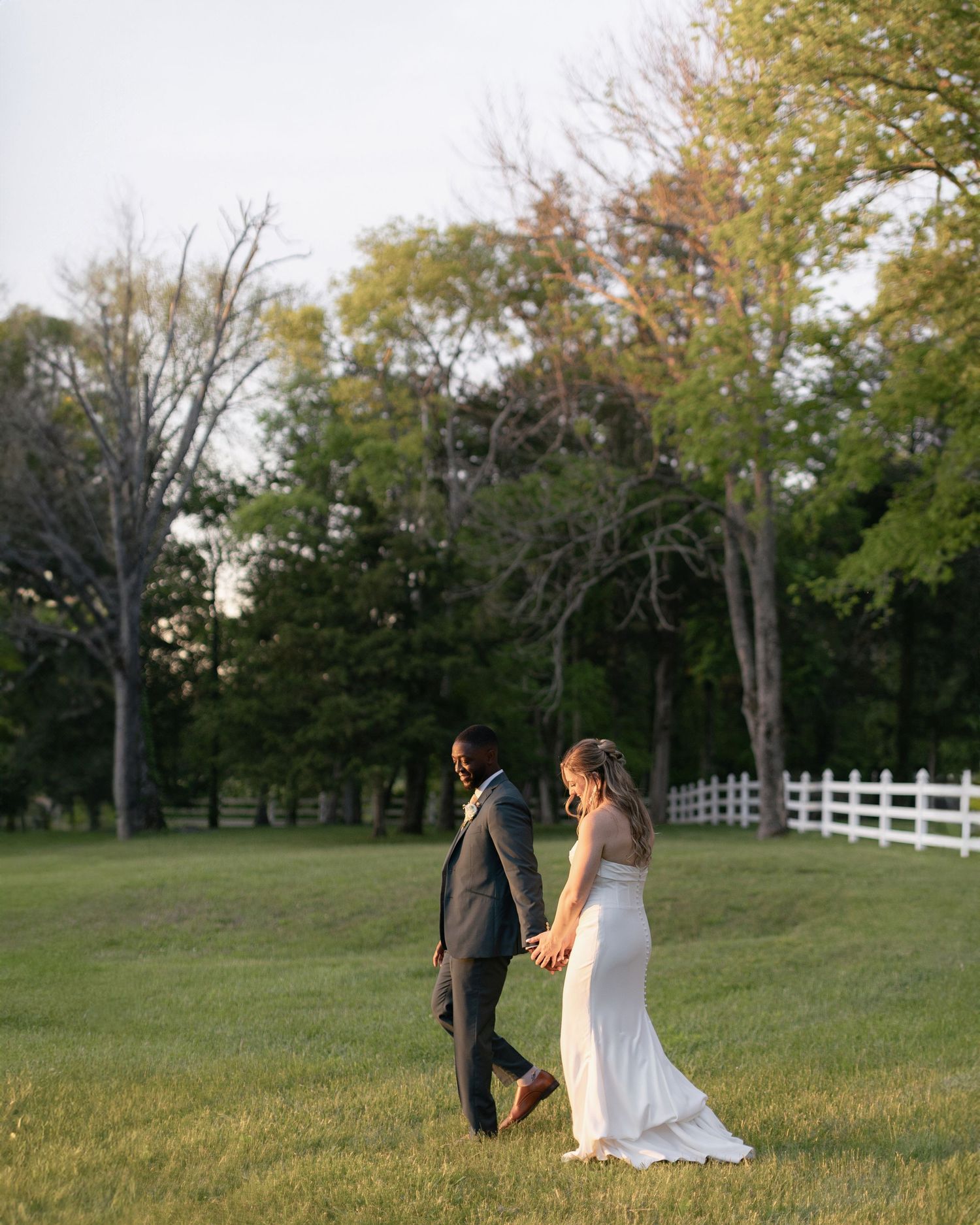 Couple walking together on lush green lawn with white fence and autumn trees in background at sunset at Legacy Farms near Nashville, TN.