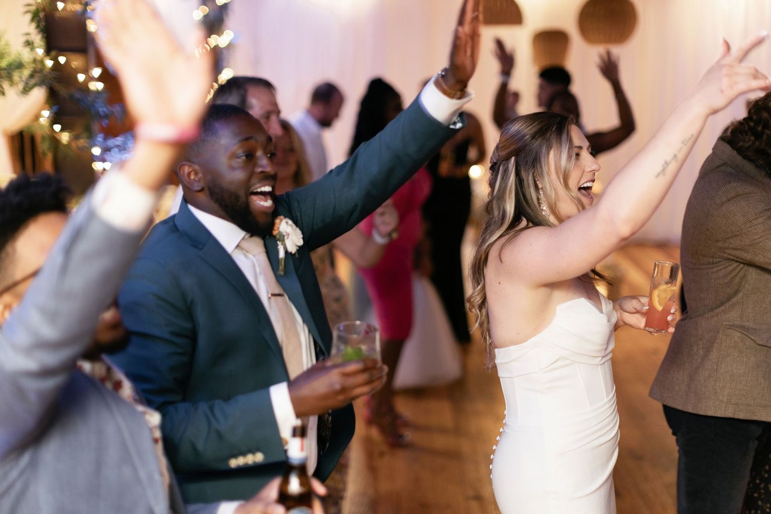 Wedding guests celebrate and dance with raised arms during a lively reception party.