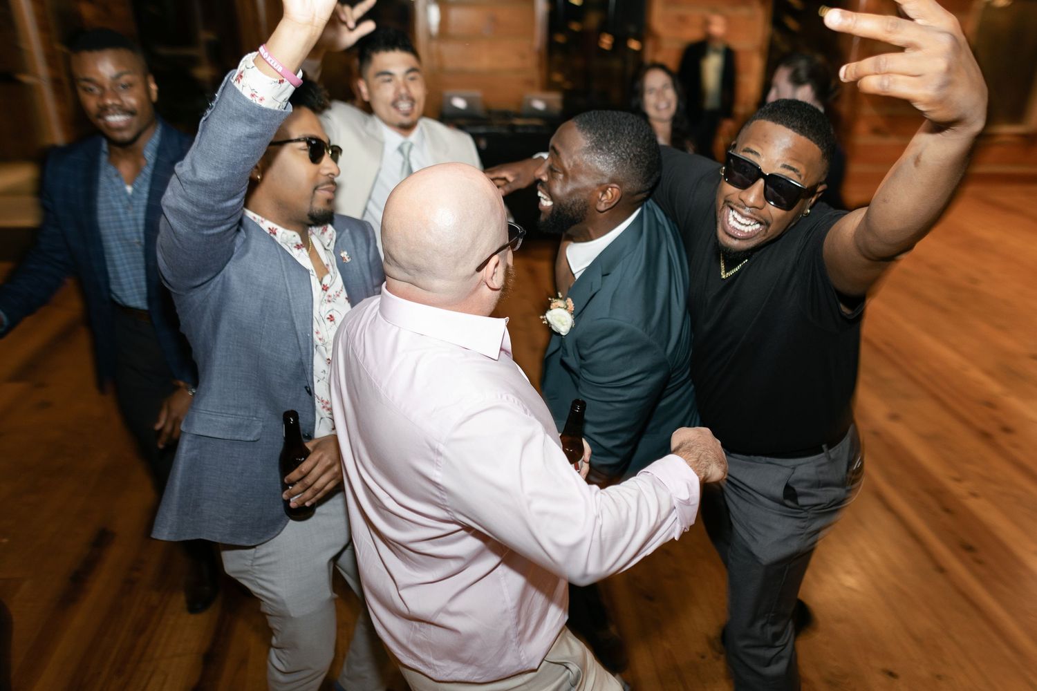 People dancing and celebrating together with raised arms on a wooden dance floor at an indoor event.