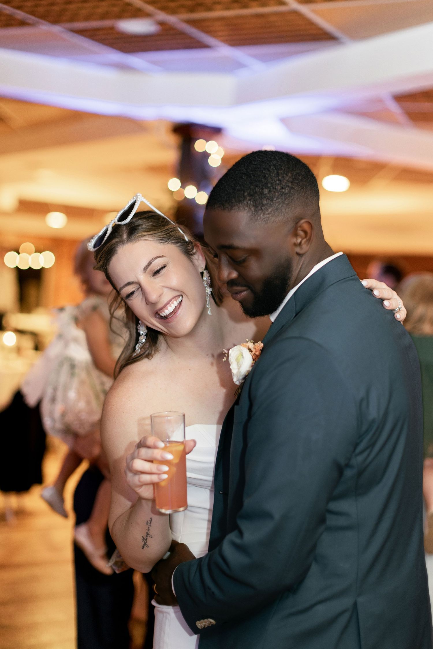 A couple shares a joyful moment together on their wedding day while holding cocktails in a reception venue.