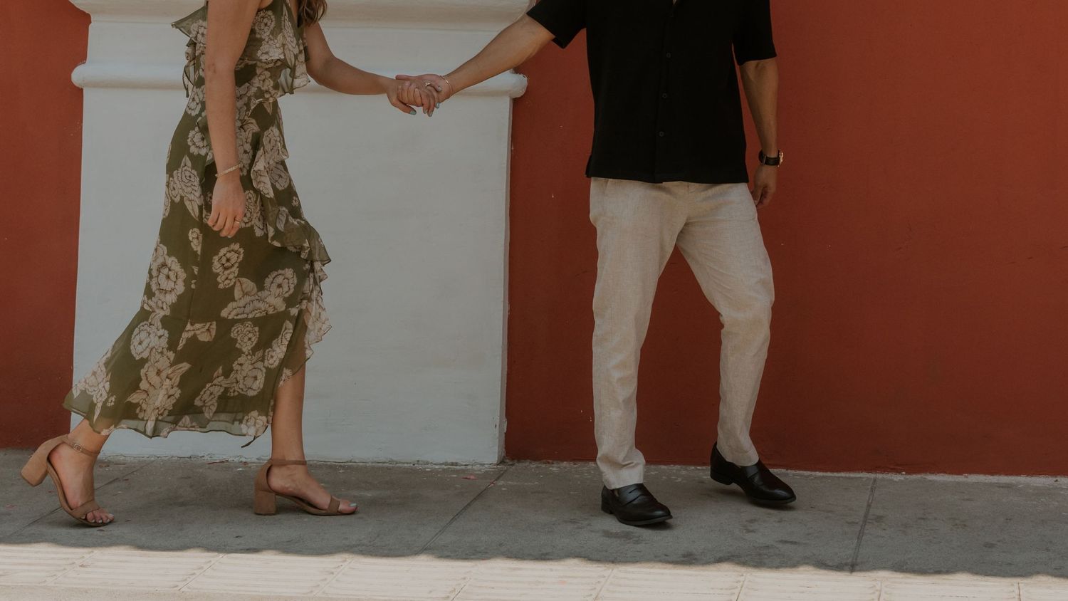 Two people standing side by side against a terra cotta wall, showing only their legs and clothing.
