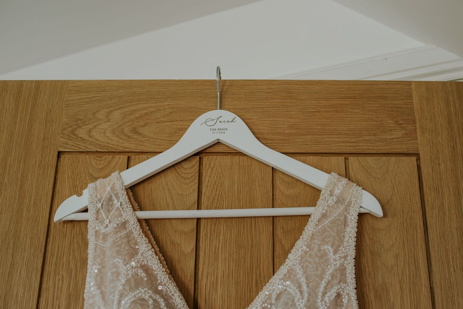 A white lace dress hanging on a wooden hanger against oak wood panel doors.