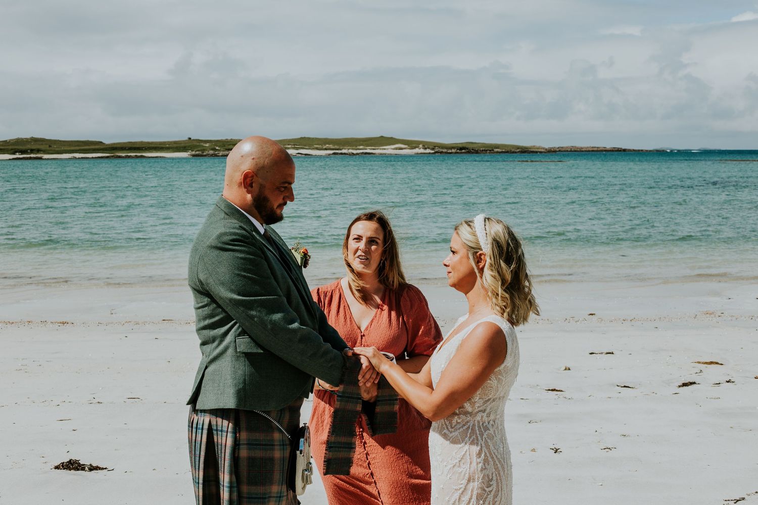 Intimate beach ceremony with traditional Scottish kilt attire against blue ocean waters.
