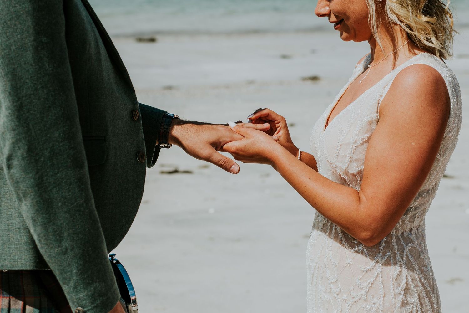 Close up of wedding ring exchange ceremony with bride holding groom's hand on beach.