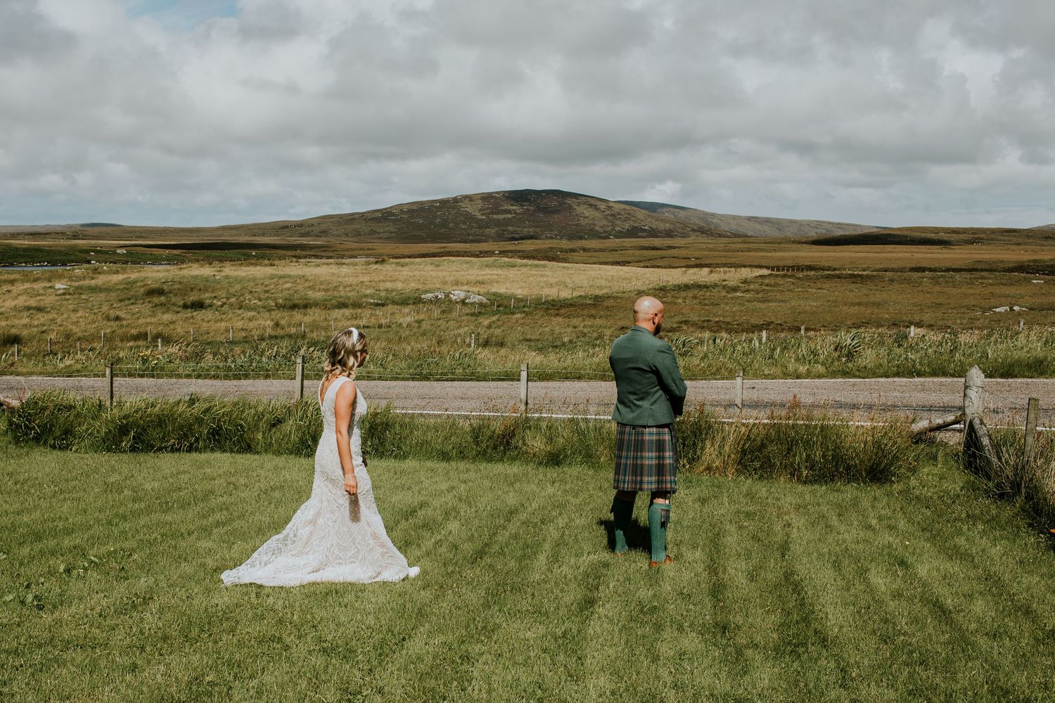 Two people stand in a green field with rolling hills and cloudy skies in the Scottish countryside.