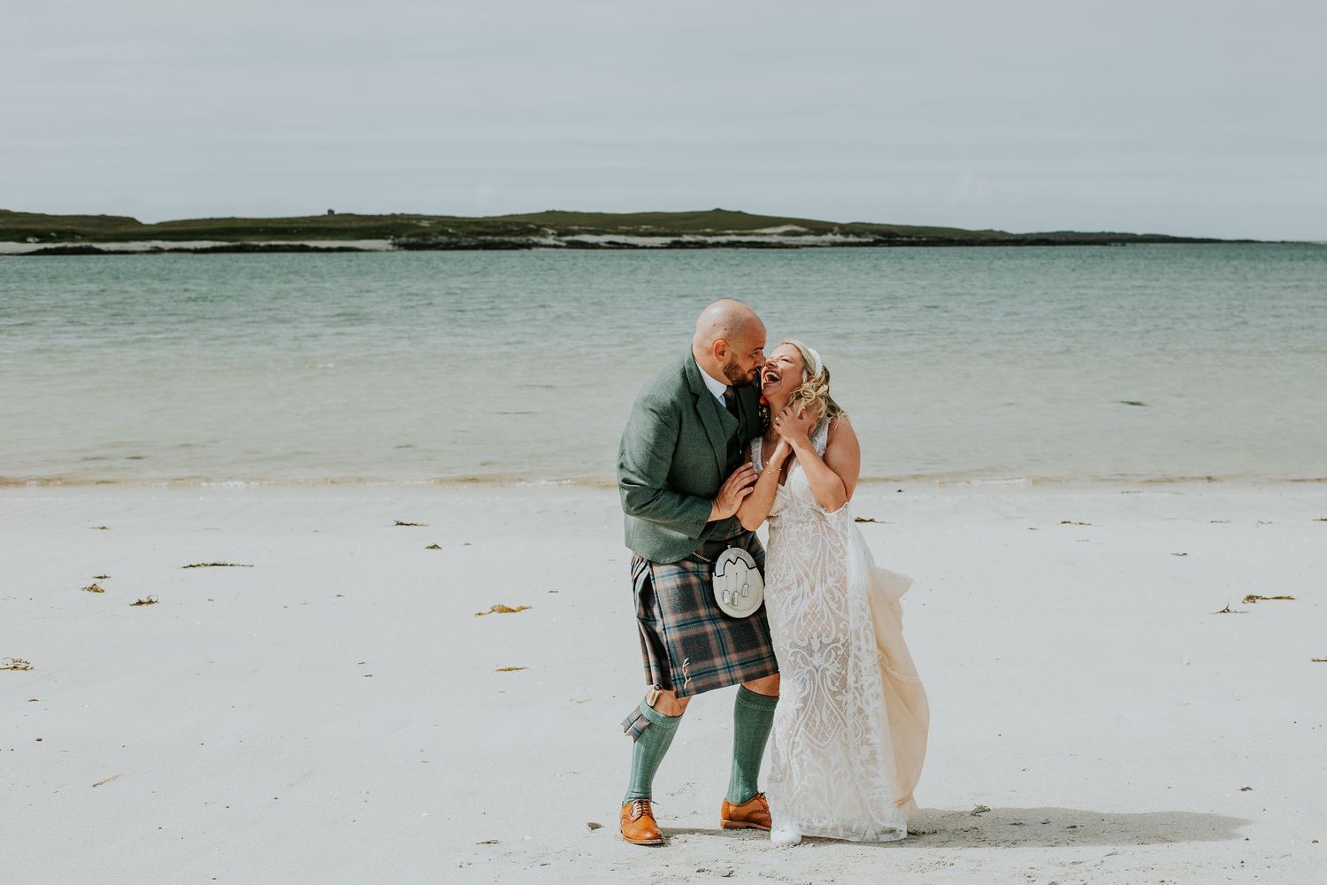Wedding couple sharing intimate moment on beach with dramatic coastal backdrop.