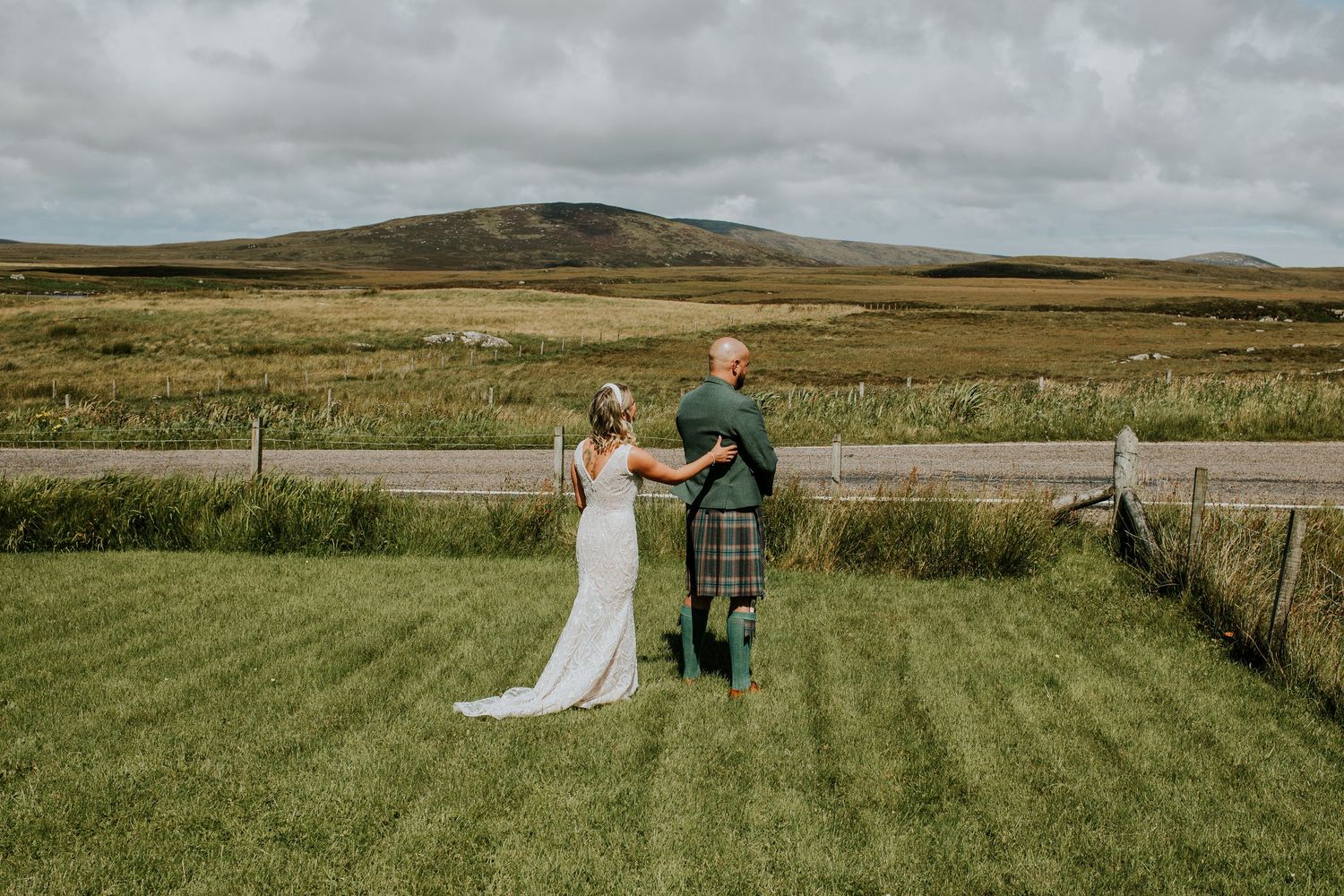 A wedding couple stands in the Scottish countryside with rolling hills and grasslands in the background.