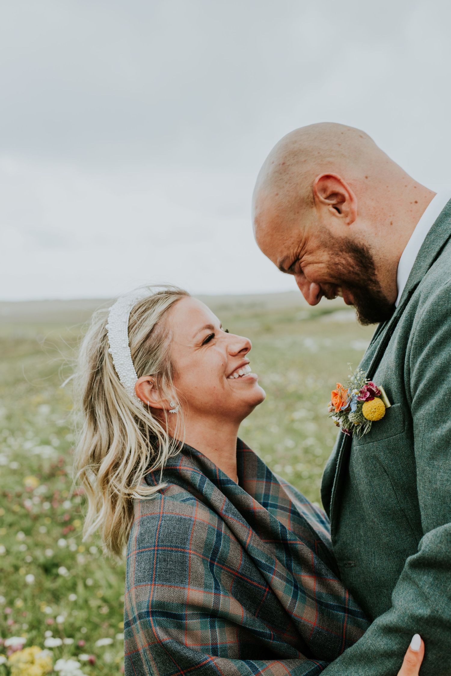 A loving couple shares a joyful moment together in a grassy field on an overcast day.
