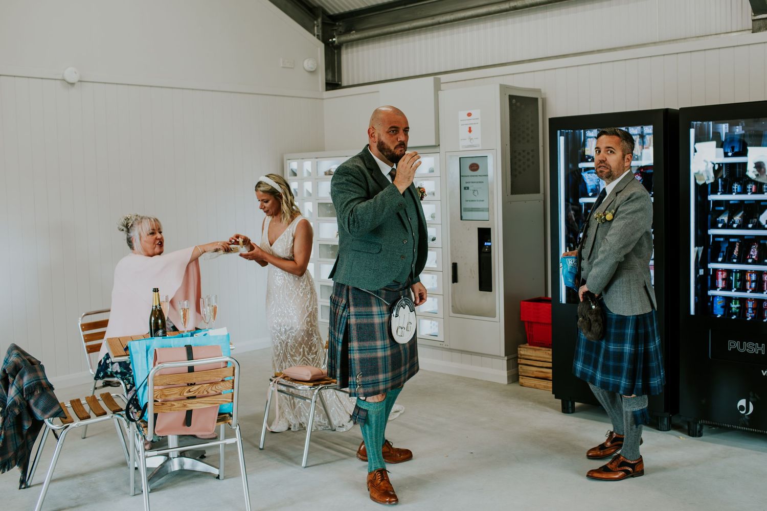 Wedding celebration in casual indoor setting with people in Scottish formal wear.