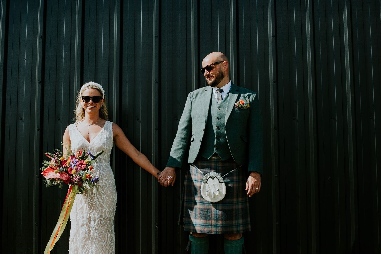 Contemporary wedding portrait against a dark backdrop featuring traditional Scottish kilt attire.