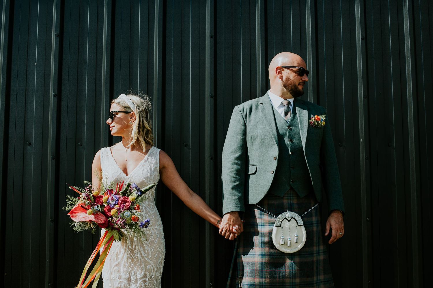 Modern wedding portrait against industrial black wall featuring Scottish wedding attire.