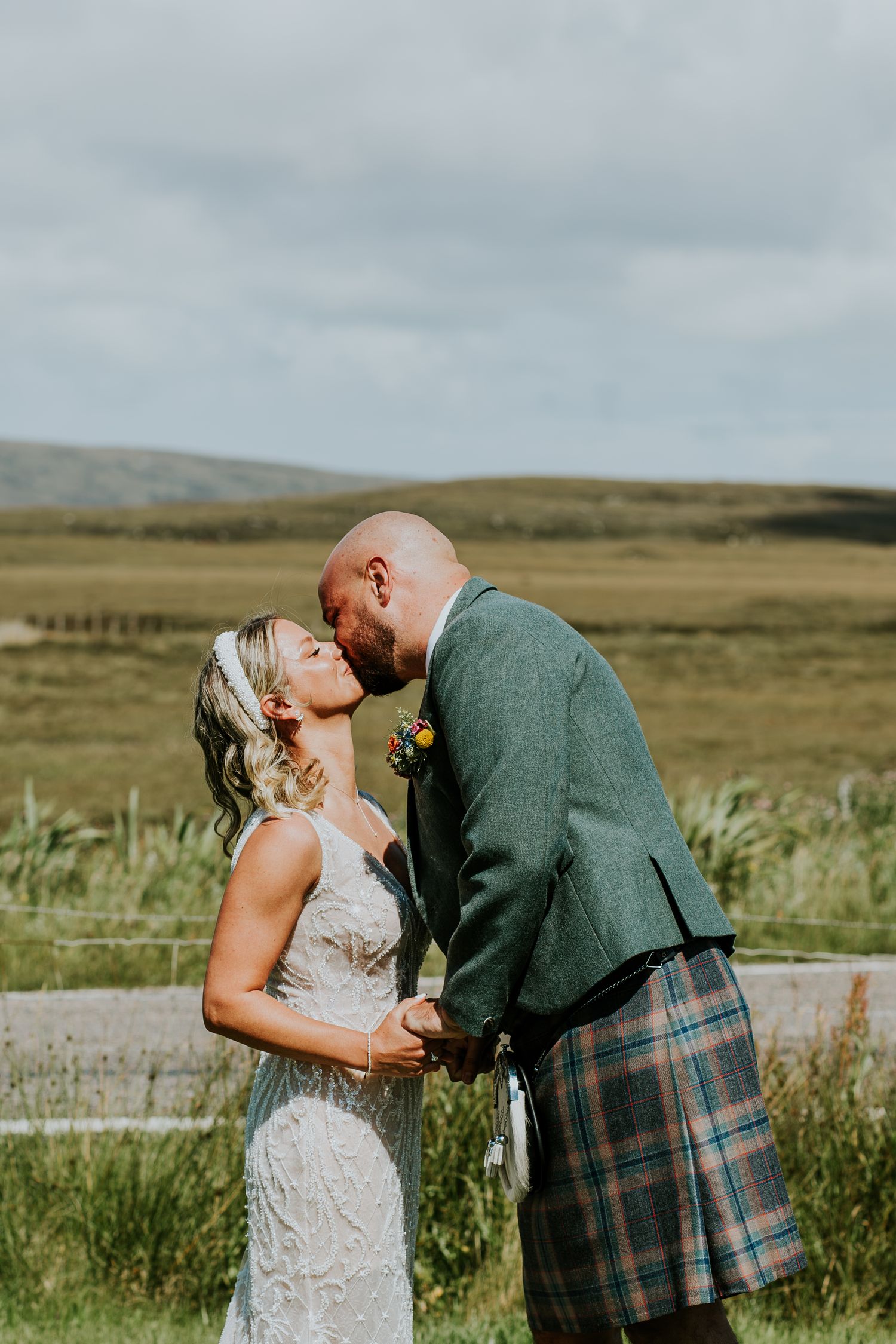 A couple shares an intimate moment in the Scottish countryside with rolling hills in the background.