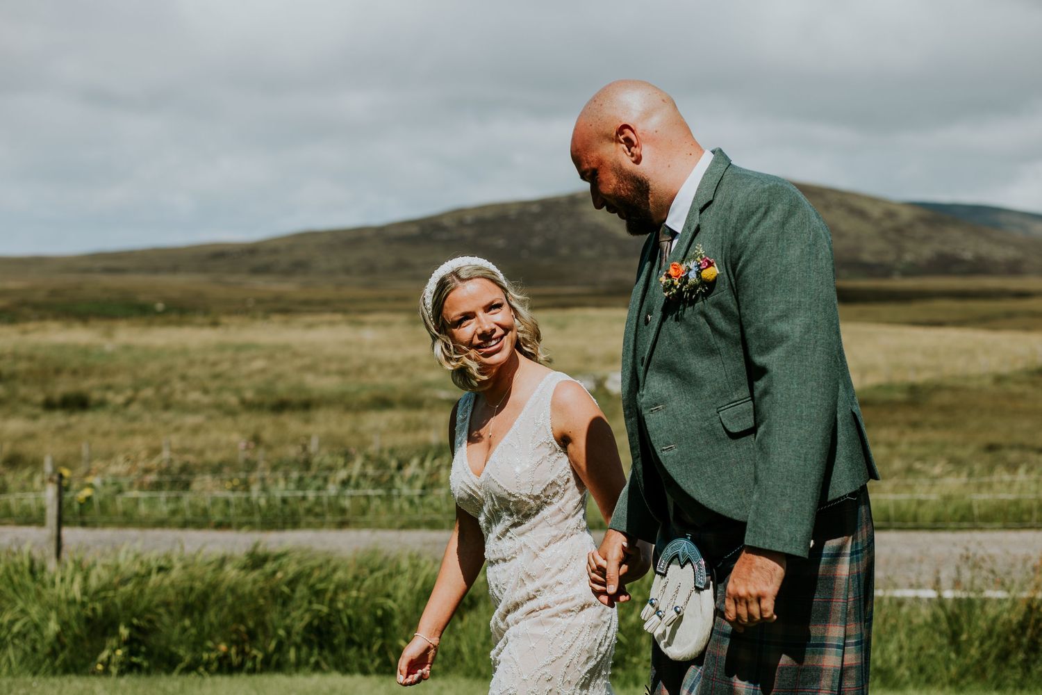 Couple in wedding attire share a joyful moment together on a scenic Scottish highland landscape.