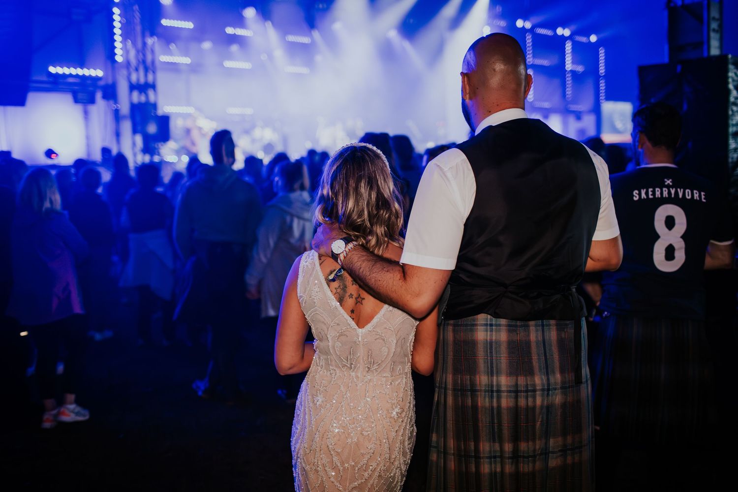 A couple embraces during a concert with atmospheric blue lighting and a crowd in the background.