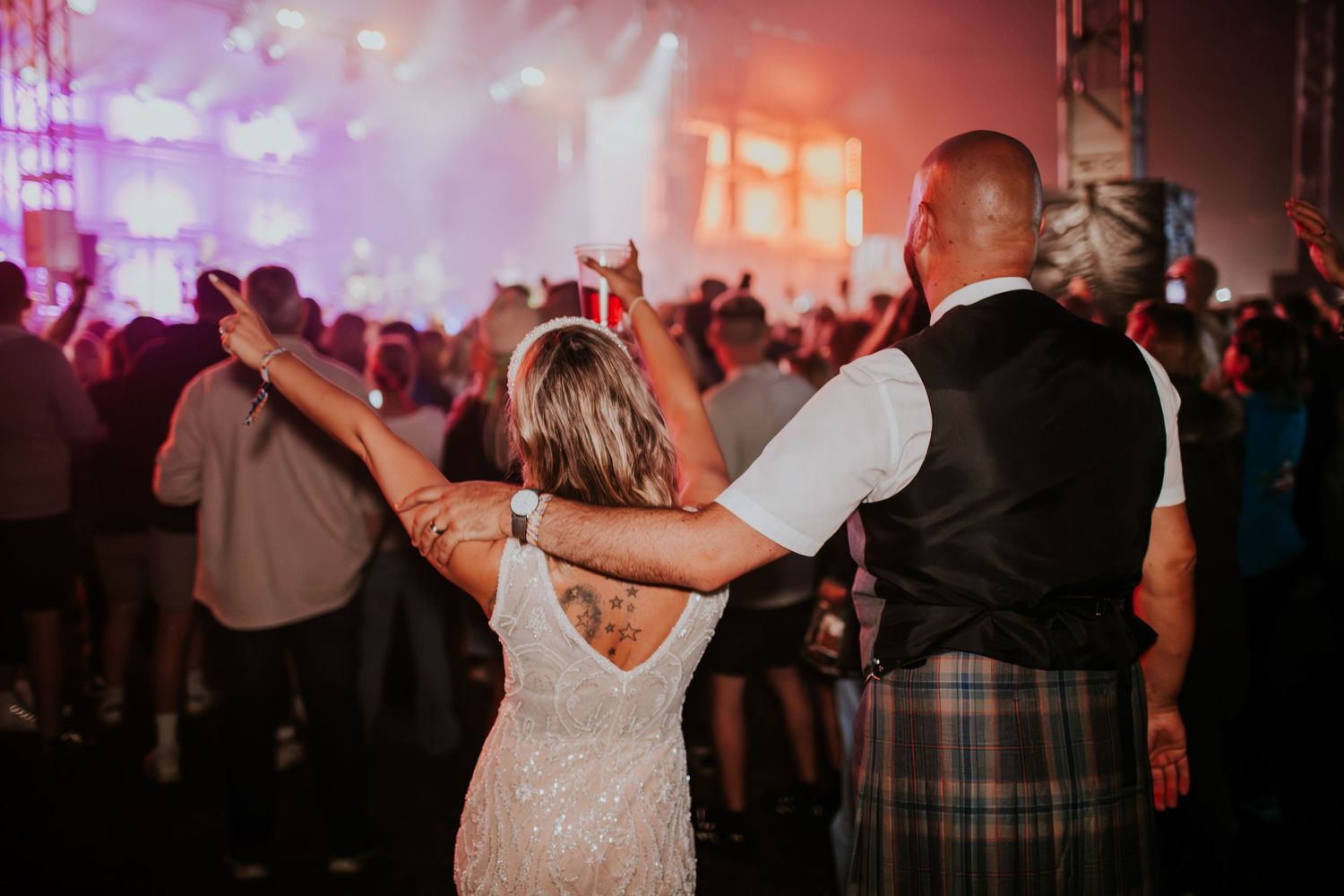 Couple dancing together at a wedding reception with atmospheric lighting and guests in the background.